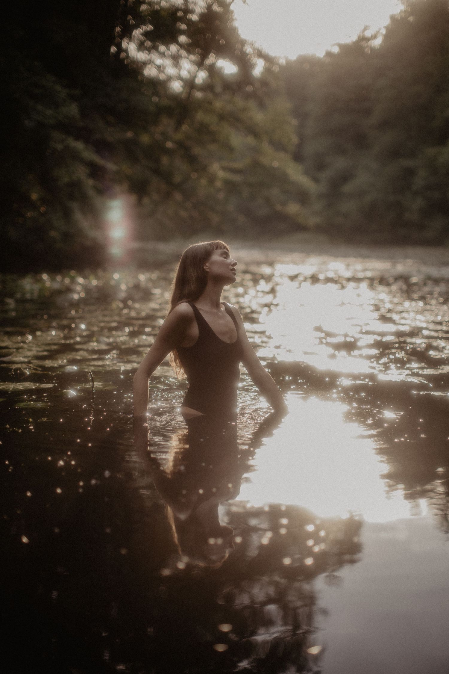 Person standing in lake at sunset with reflective water and dreamy atmosphere.