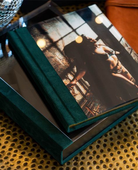 Softly lit photograph book with green velvet cover and romantic lighting strings reflected on glossy pages.