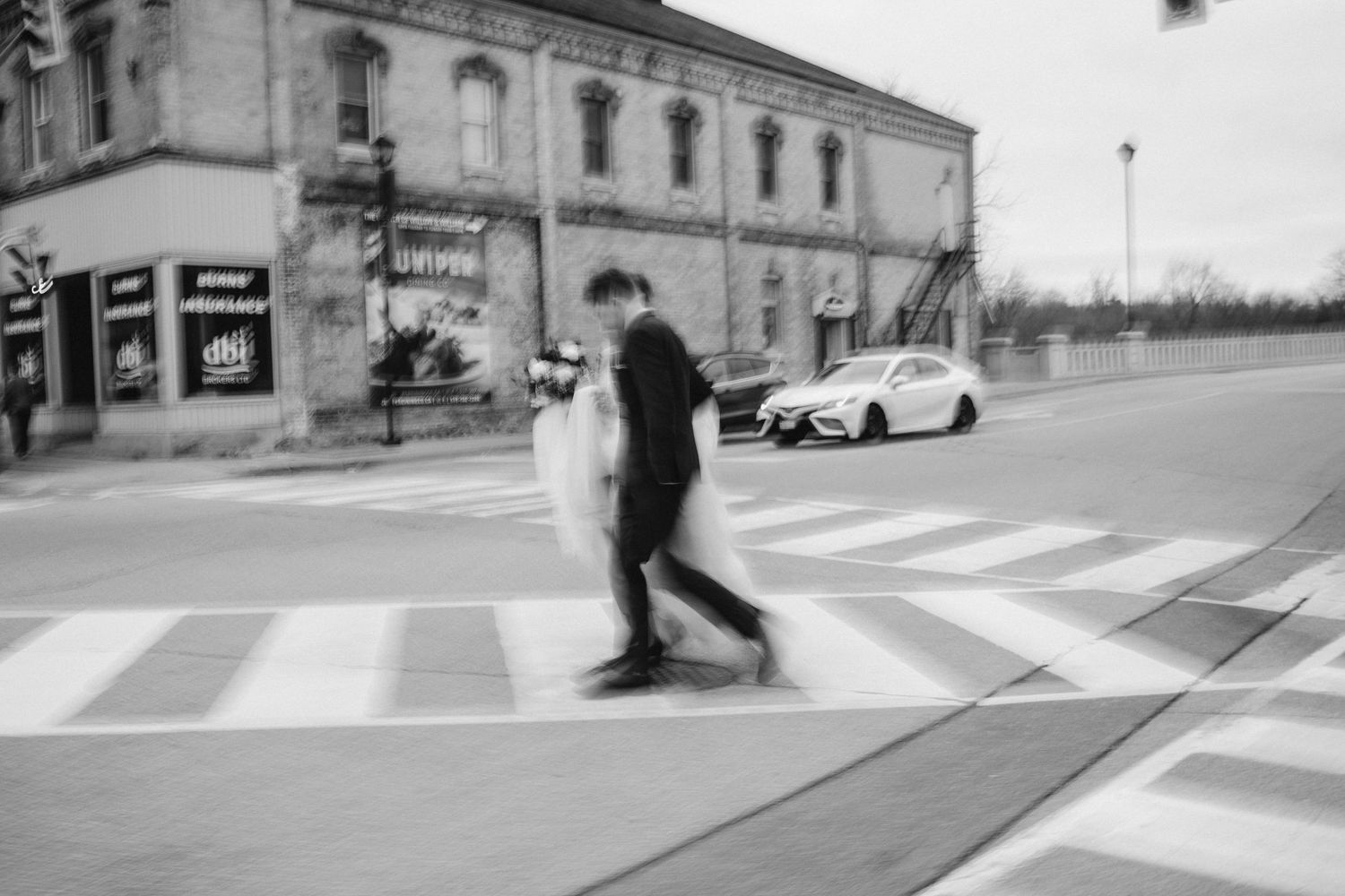 A blurred black and white street photo of someone crossing an urban intersection.