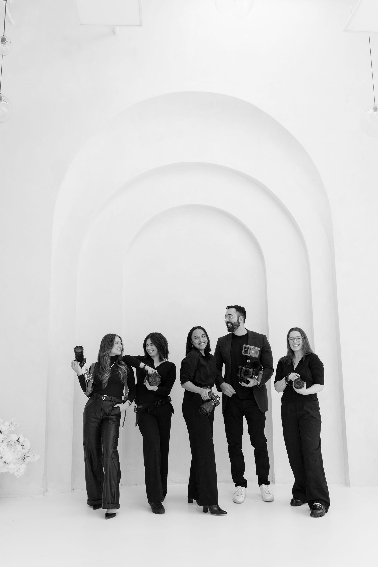 A group in black attire stands in an arched white room creating a minimalist artistic composition.