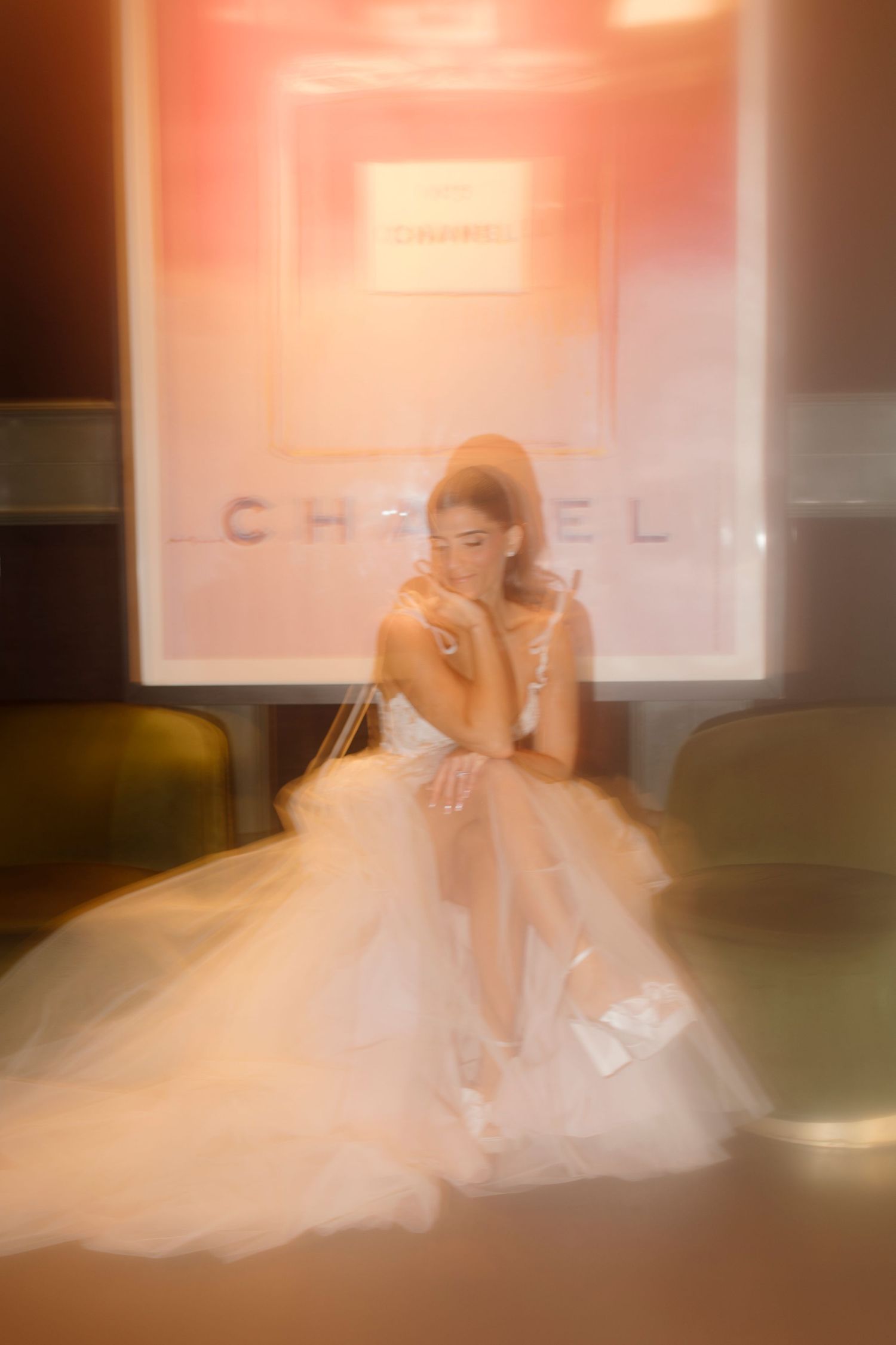 Dreamy soft-focus photo of a figure in an elegant white tulle gown seated in front of a Chanel backdrop.