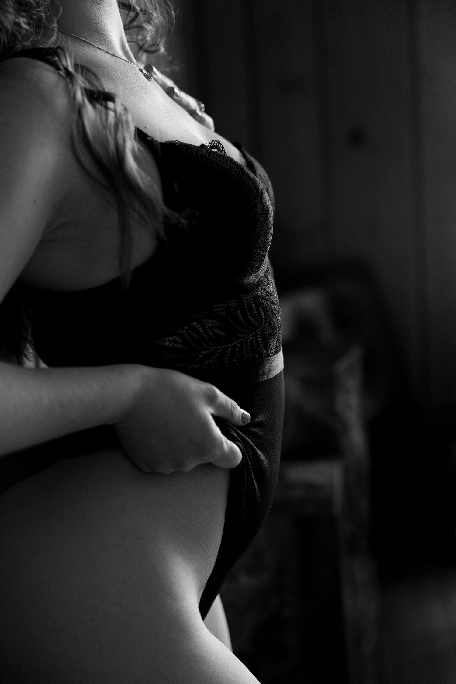 Black and white artistic boudoir photo showing torso in lace lingerie with moody lighting and soft focus effect.