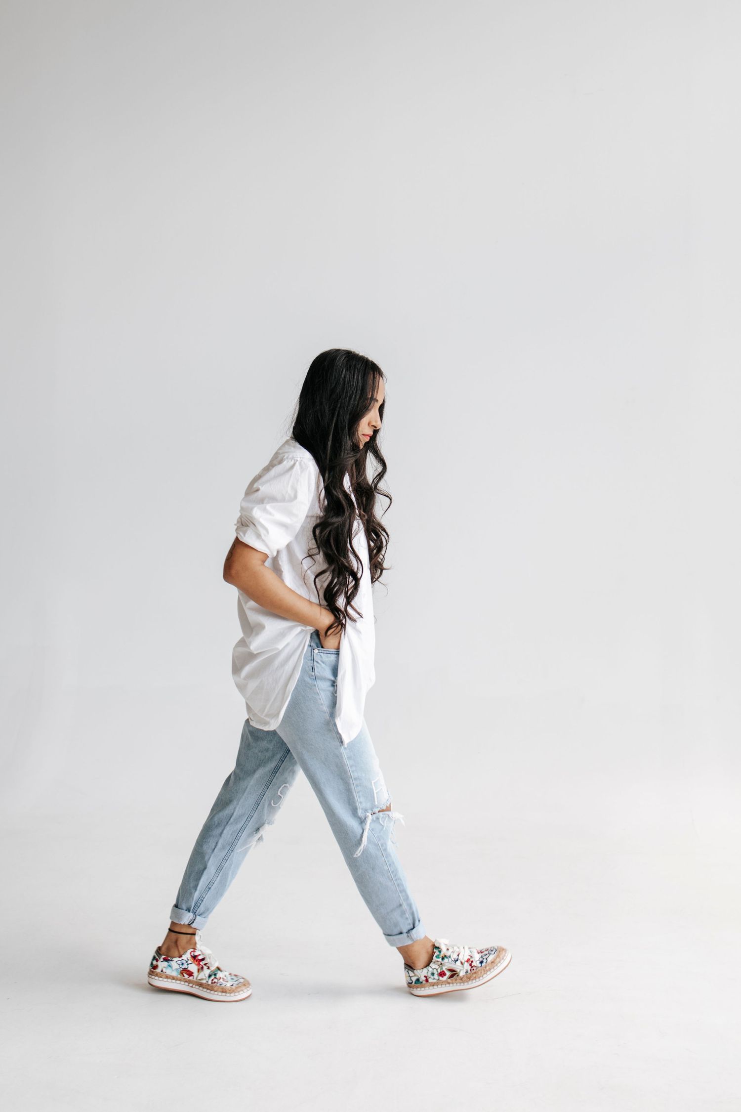Person in white shirt and ripped jeans walking confidently while wearing floral sneakers.