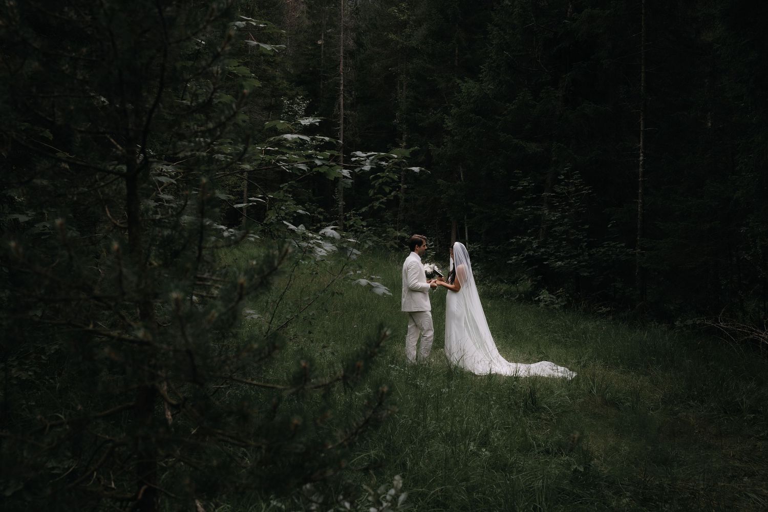 A couple in wedding attire stands together in a lush forest setting during their outdoor ceremony.