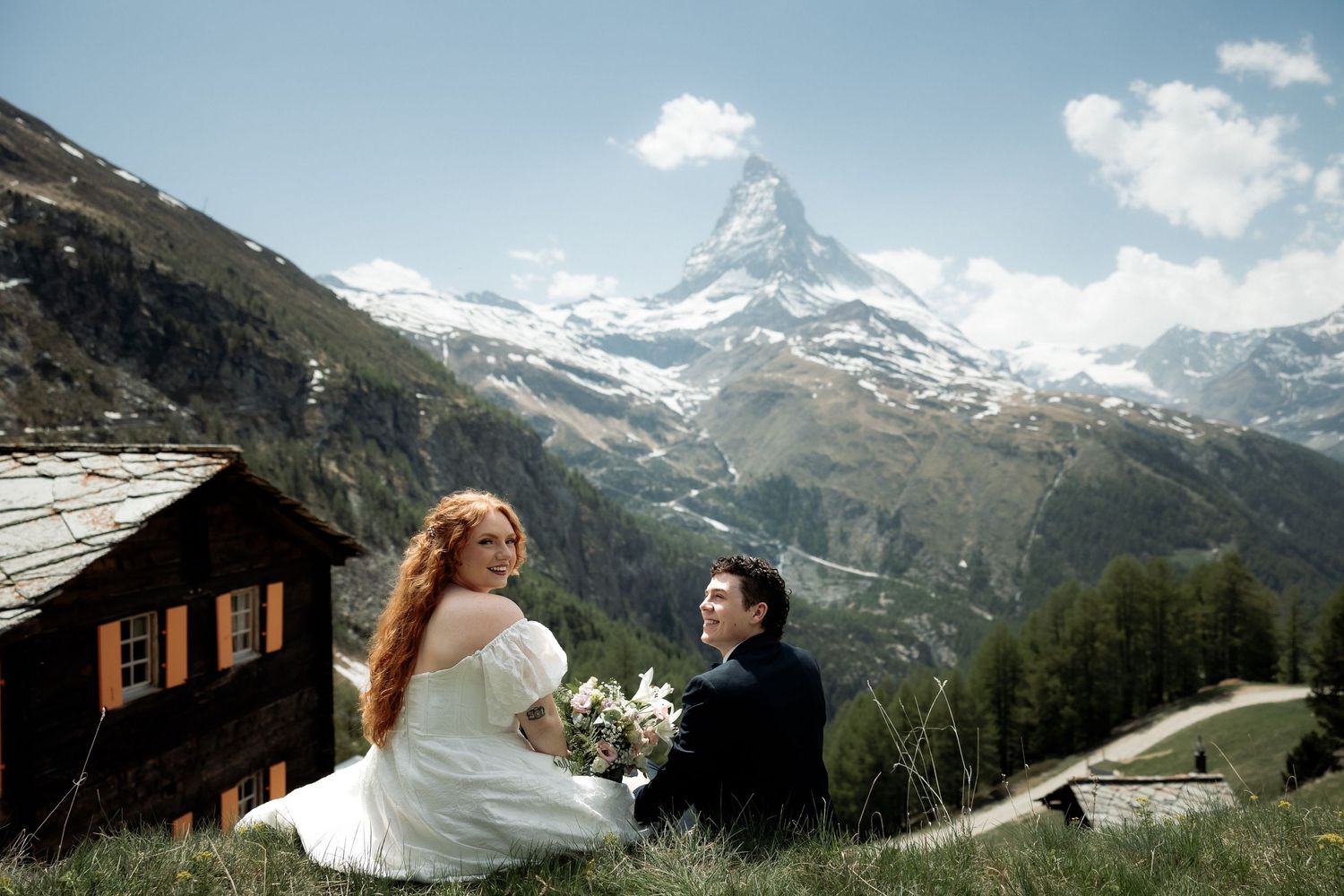 Bride and groom sitting on alpine meadow with iconic Matterhorn peak backdrop in Zermatt, Switzerland.