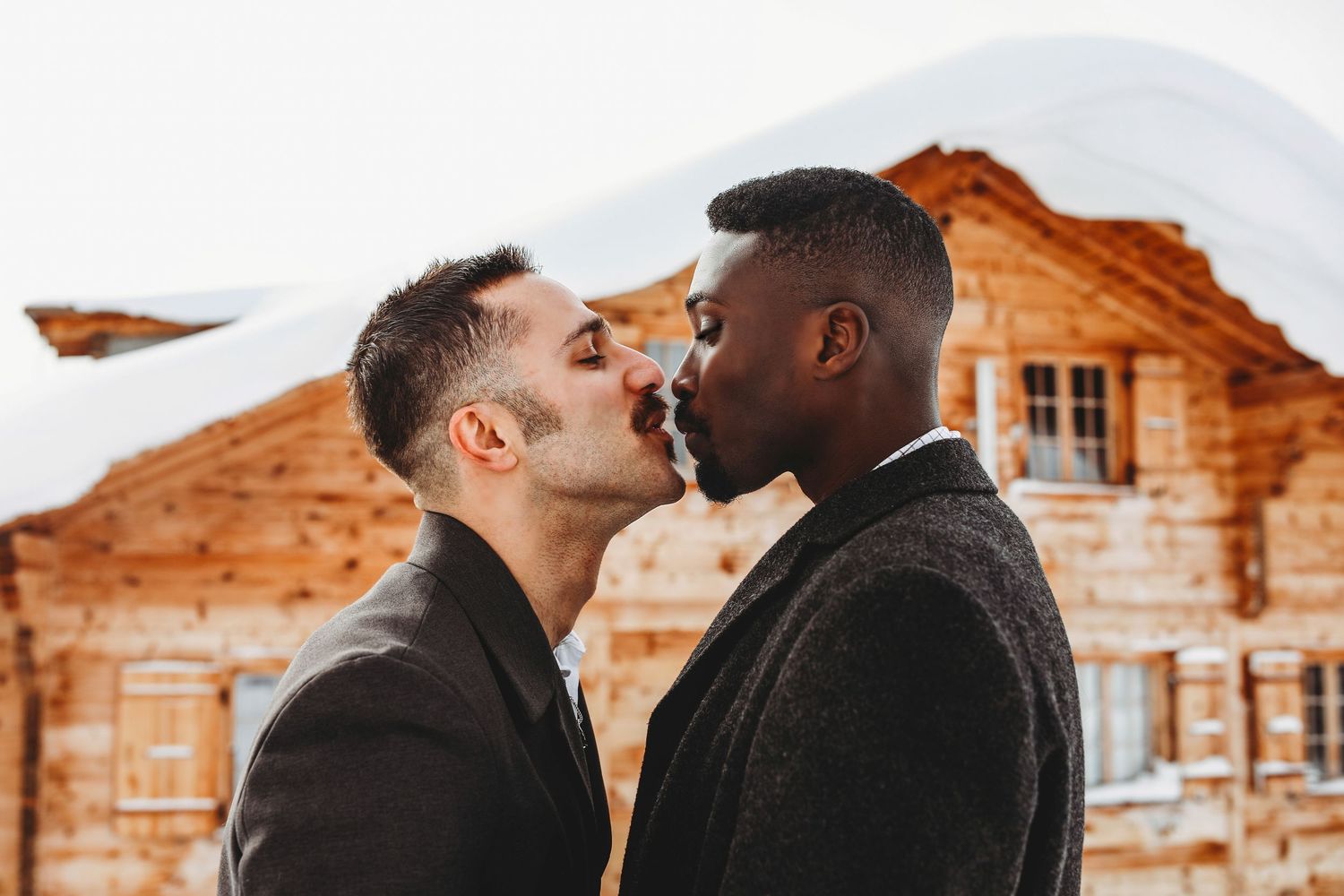A romantic couple embracing in front of rustic wooden cabins during sunset.