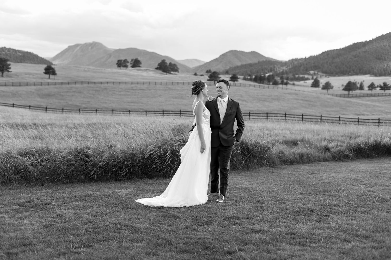 Bride and groom share romantic moment in black and white photo with scenic mountain and field backdrop.