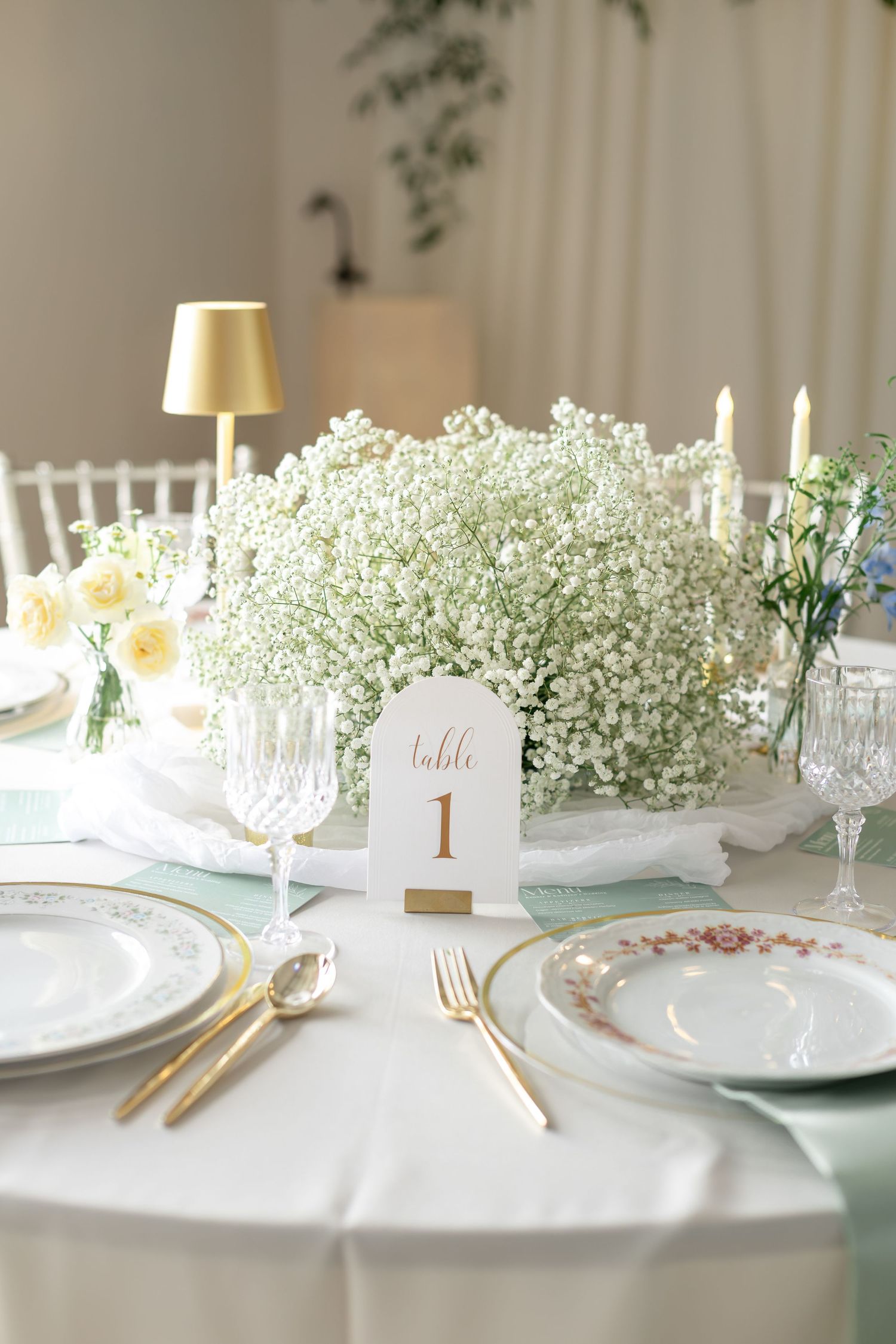 Elegant wedding table setting with babys breath centerpiece, gold cutlery, and Table 1 card.