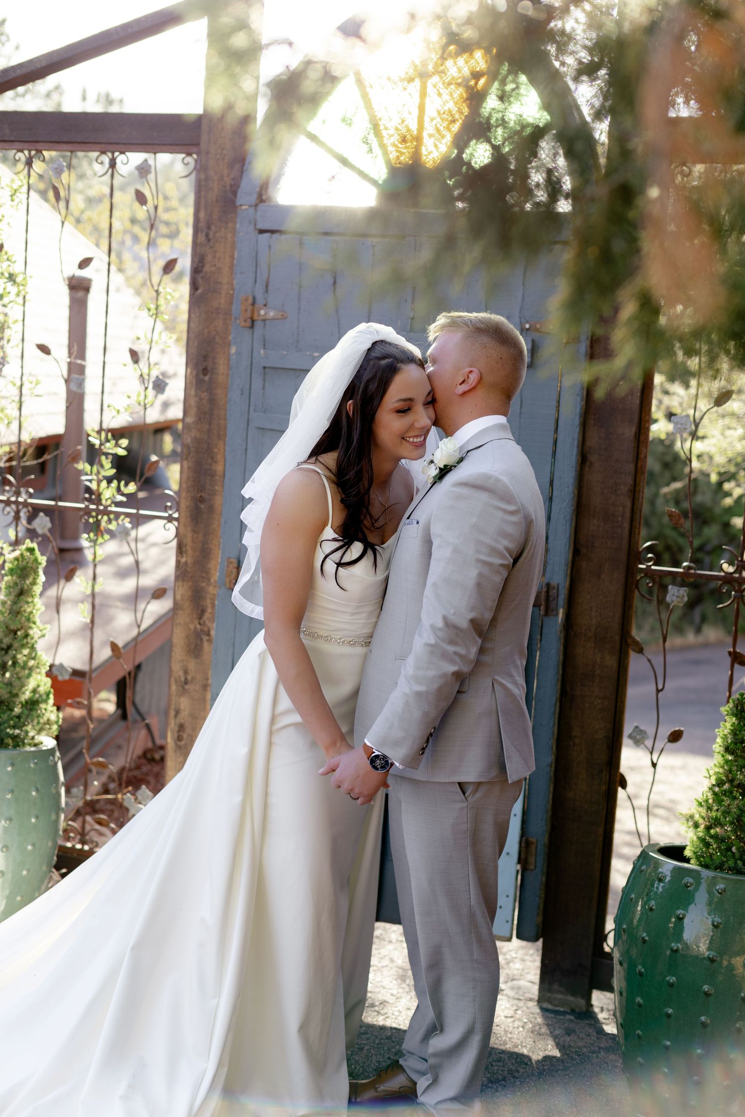 Bride and groom share romantic moment at rustic garden gate on wedding day.