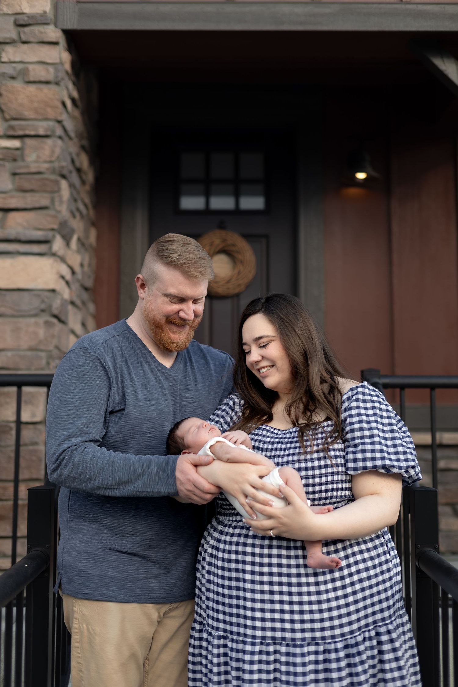 Happy couple smiling at newborn baby on home front porch, new family portrait photo.