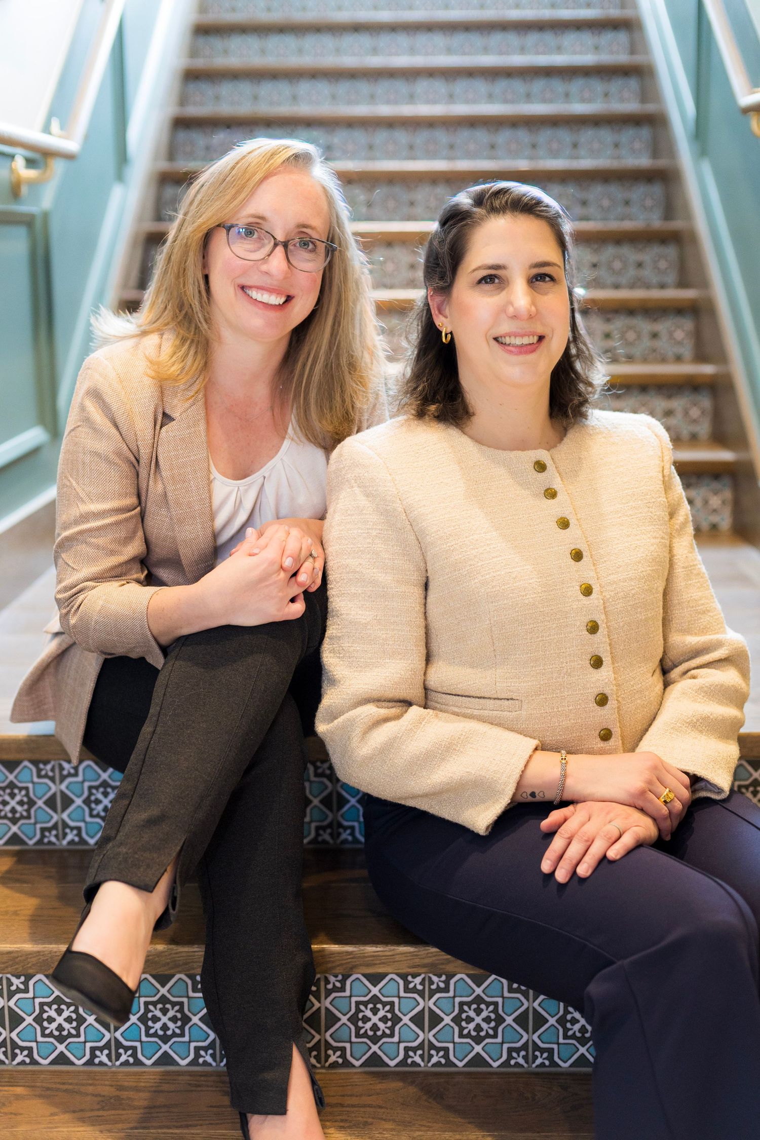 Two people sit together on decorative tiled stairs wearing contrasting light and dark outfits.
