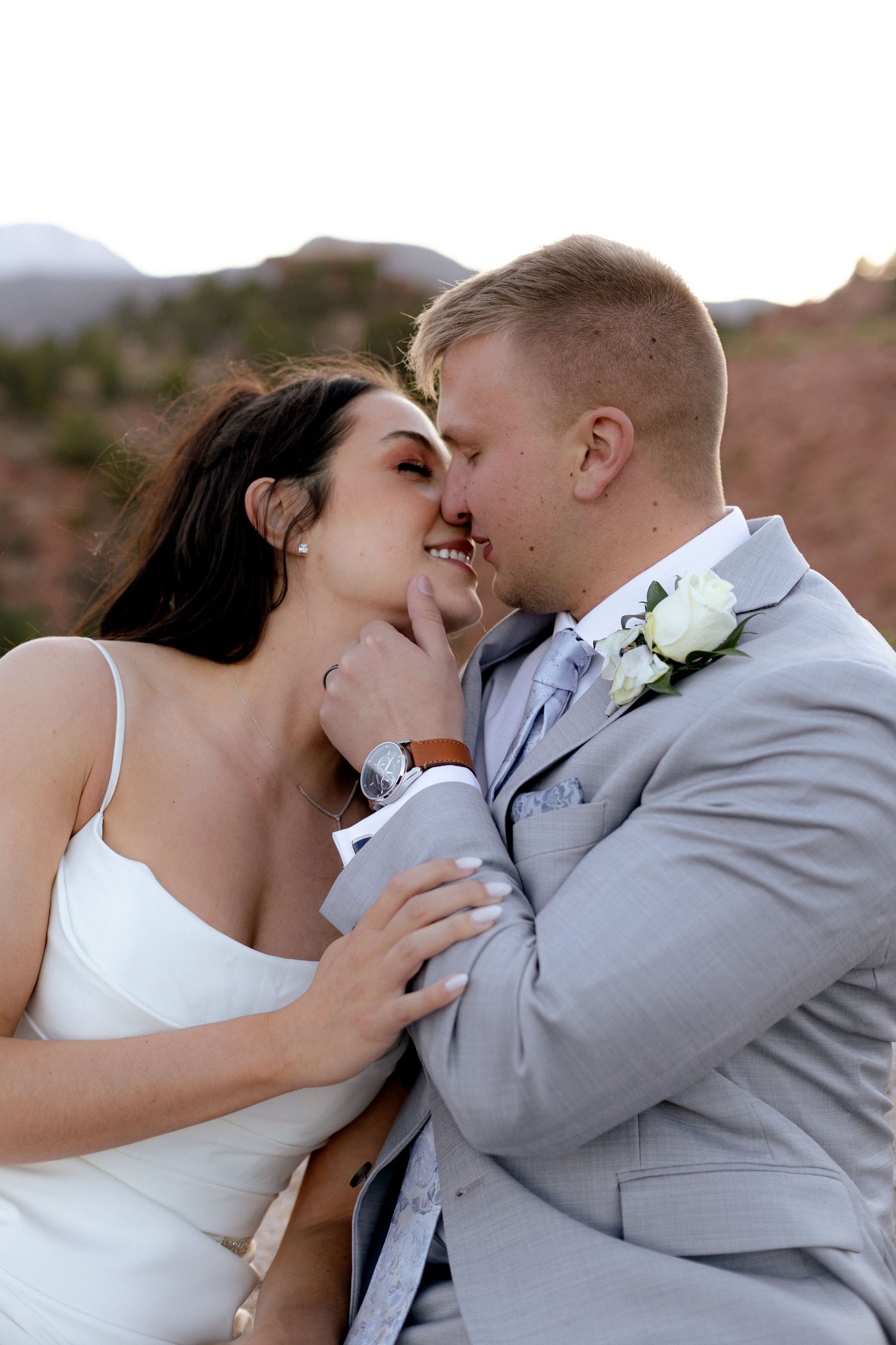 Bride and groom share a romantic kiss at sunset with red rock mountains in the background.