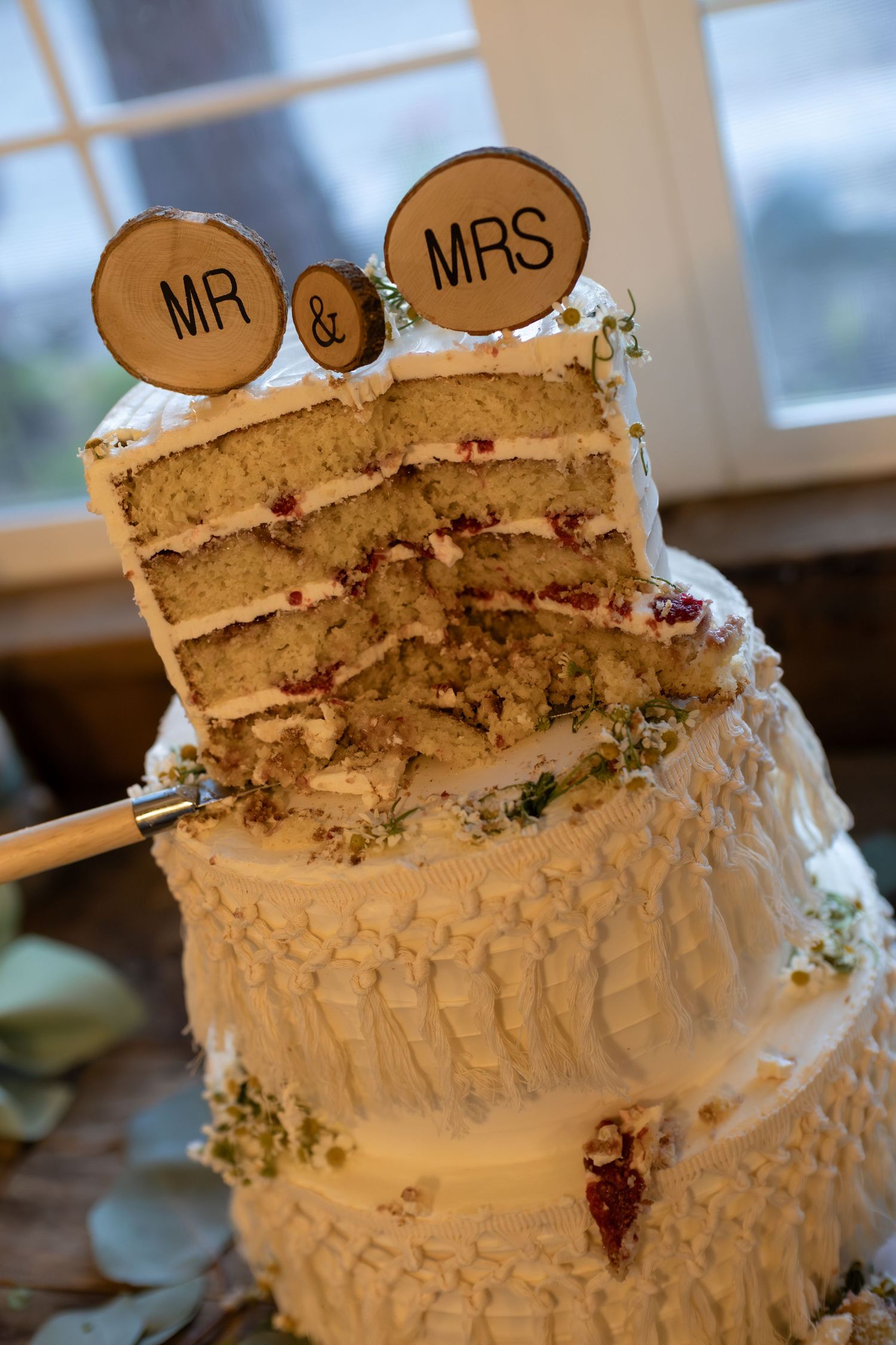 Sliced three-tier white wedding cake with Mr and Mrs wooden topper revealing layers with red filling.
