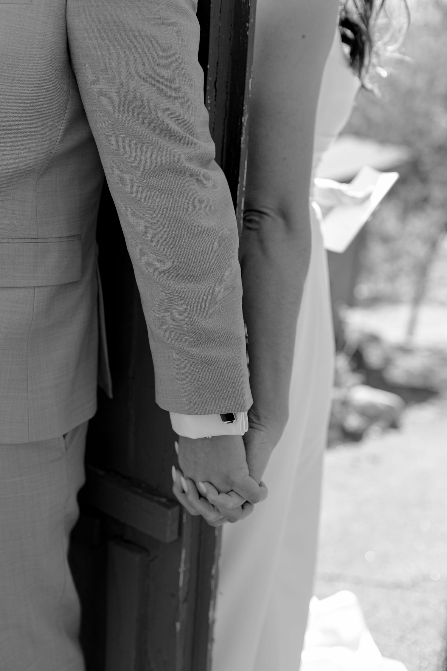 Black and white photo of bride and groom holding hands during outdoor wedding ceremony.