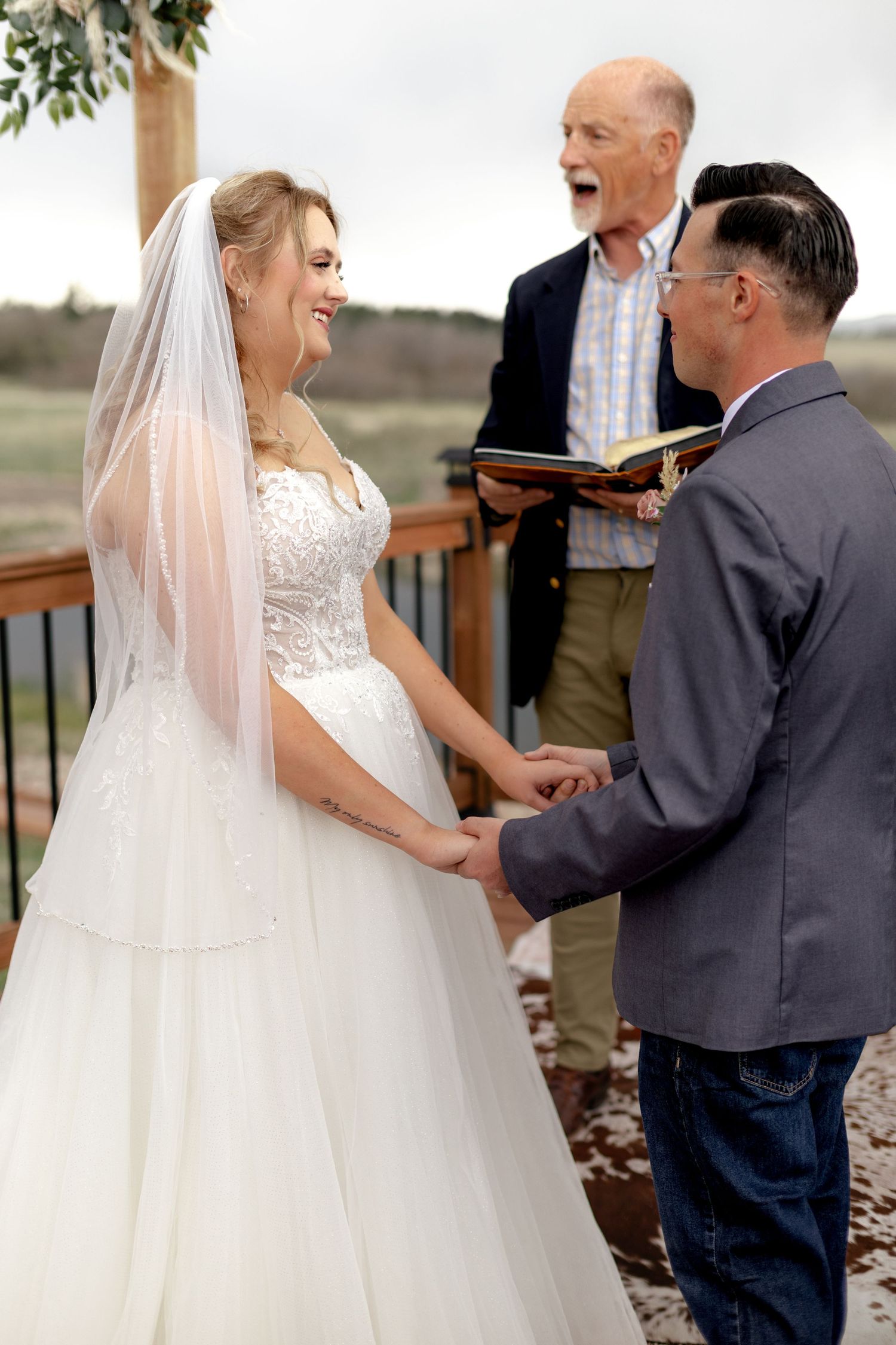 Bride and groom holding hands and smiling during outdoor wedding ceremony with officiant.