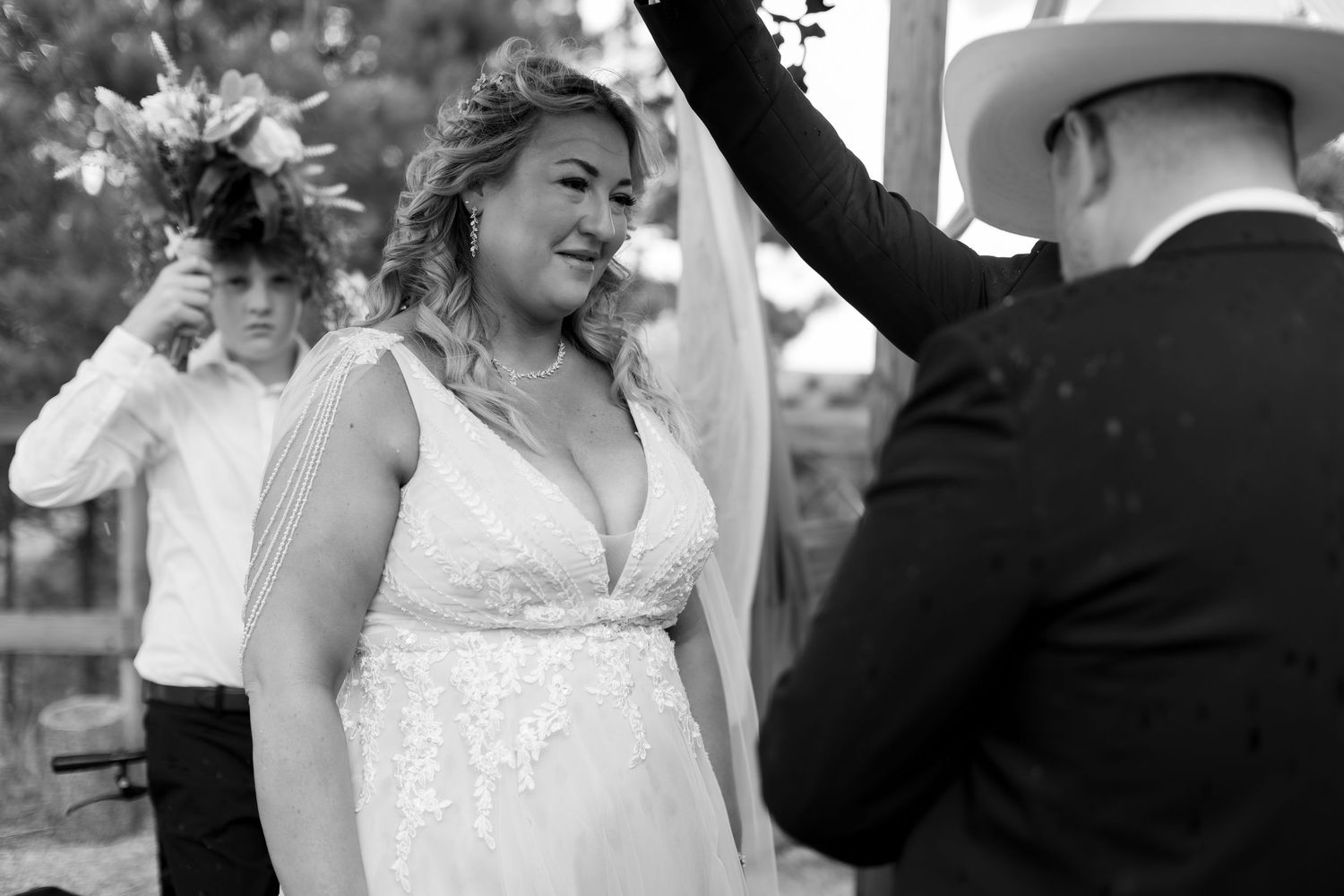 Black and white photo of emotional bride in lace gown at outdoor wedding ceremony altar.