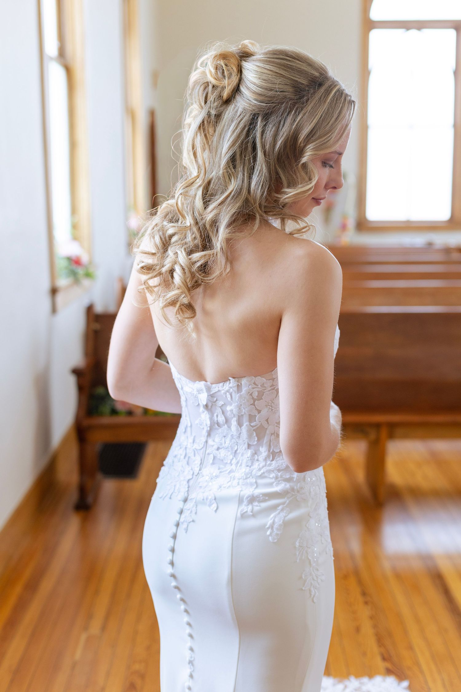 Back view of bride in white lace halter wedding gown with curled half-up hairstyle in a chapel.