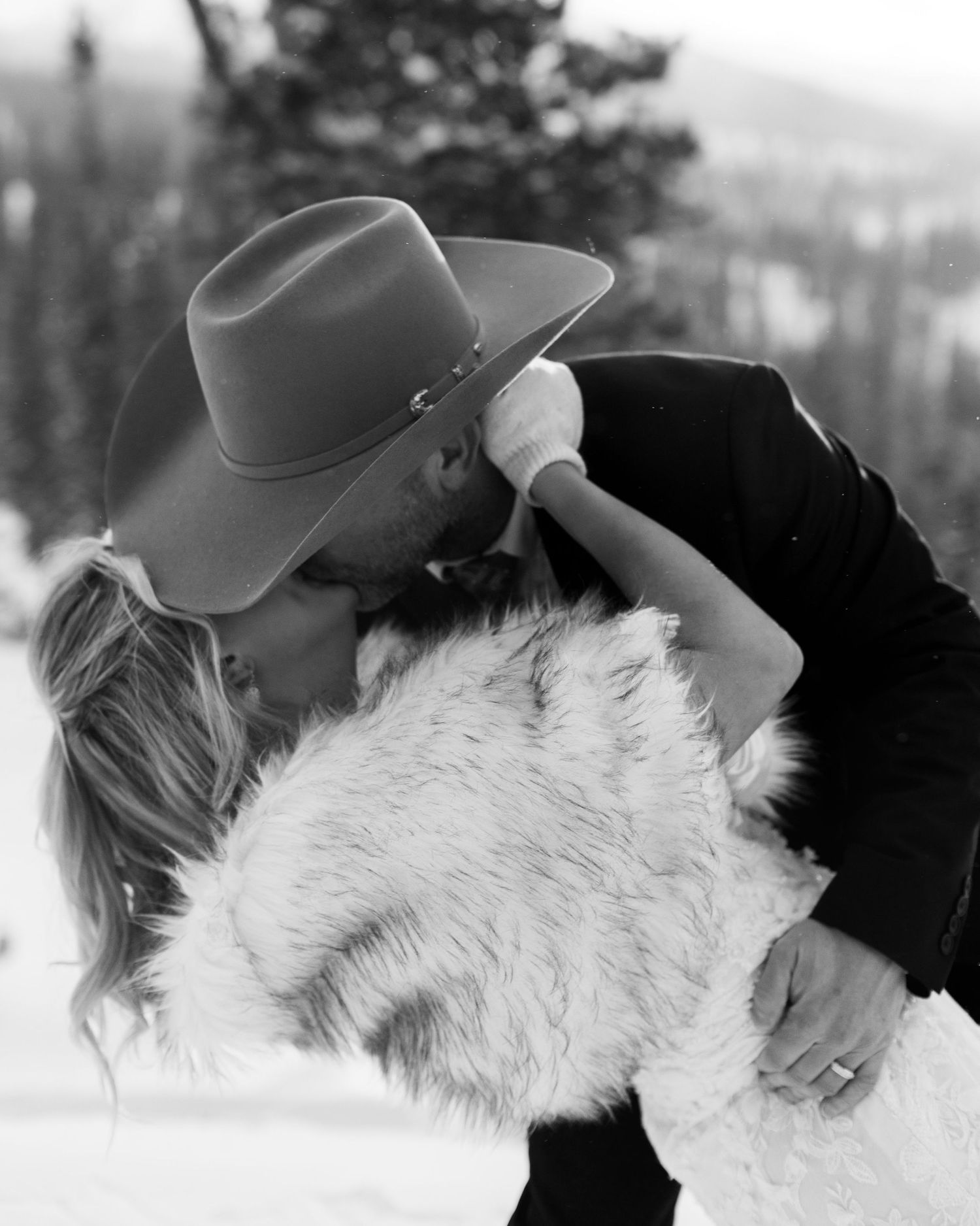 Black and white winter scene showing a person kissing a fluffy white dog in the snow.