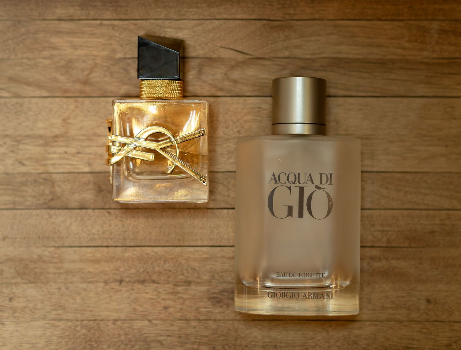 YSL Libre Intense and Acqua di Gio cologne bottles displayed on a wooden surface.