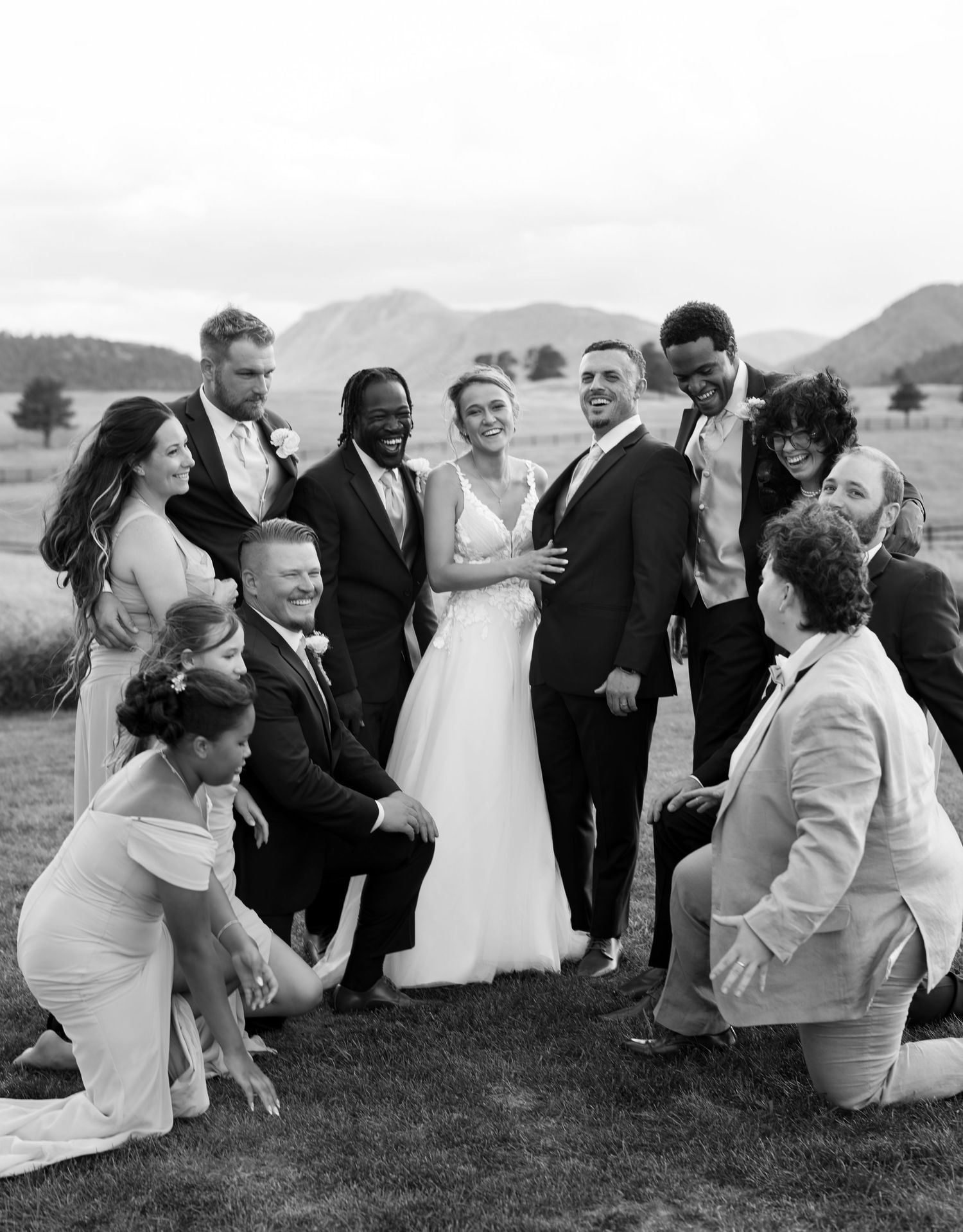 Bride and groom celebrating with diverse wedding party outdoors with scenic mountain backdrop.