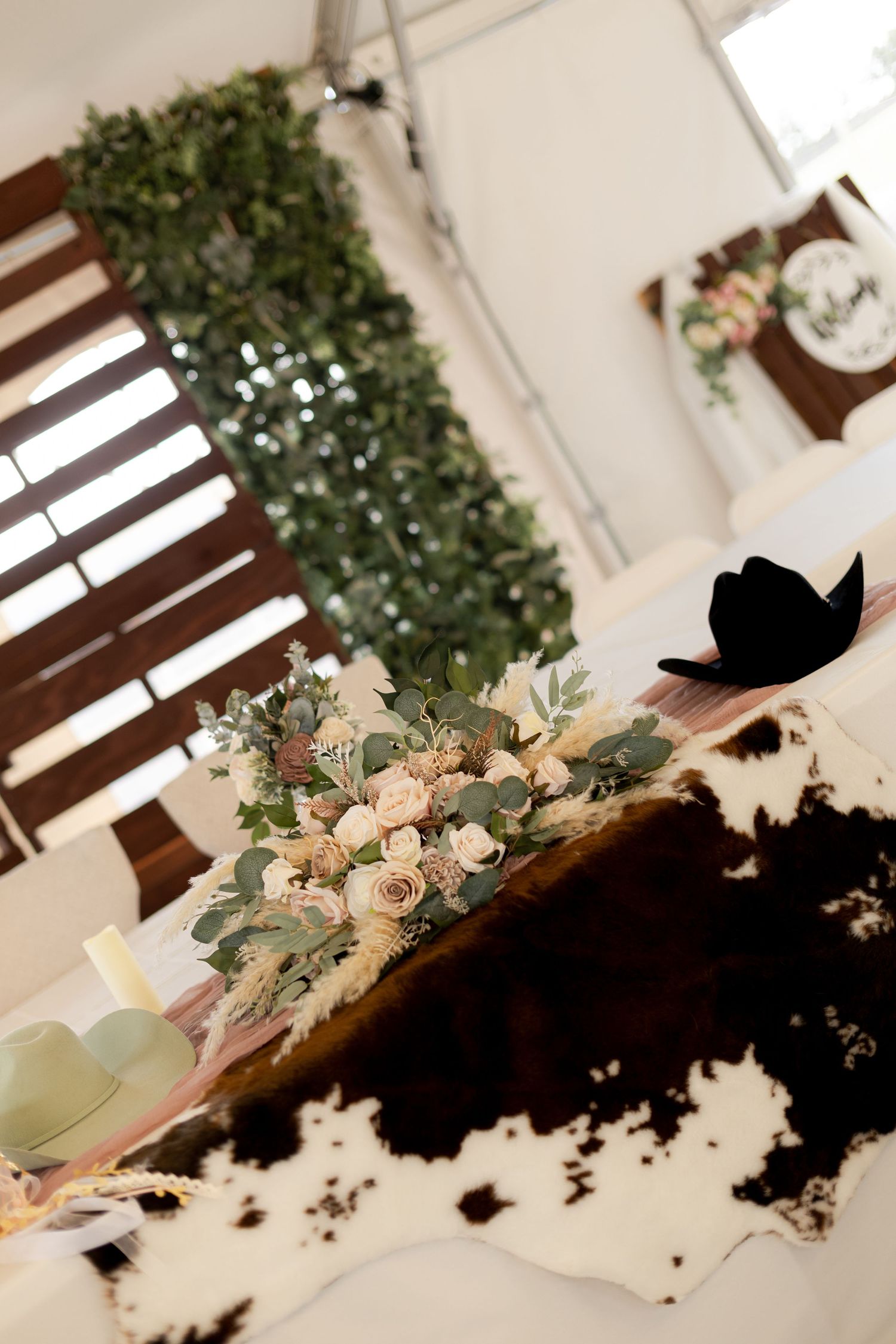 Elegant wedding reception table with blush floral centerpiece on cowhide print tablecloth under a tent.