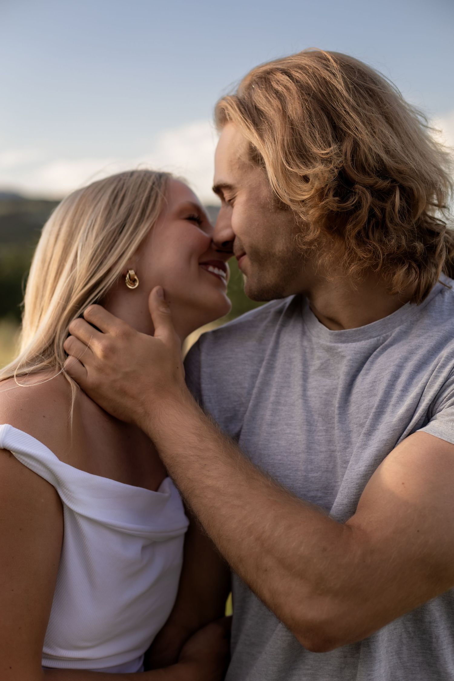 A romantic couple sharing a tender moment outdoors, smiling and about to kiss in a scenic natural setting.