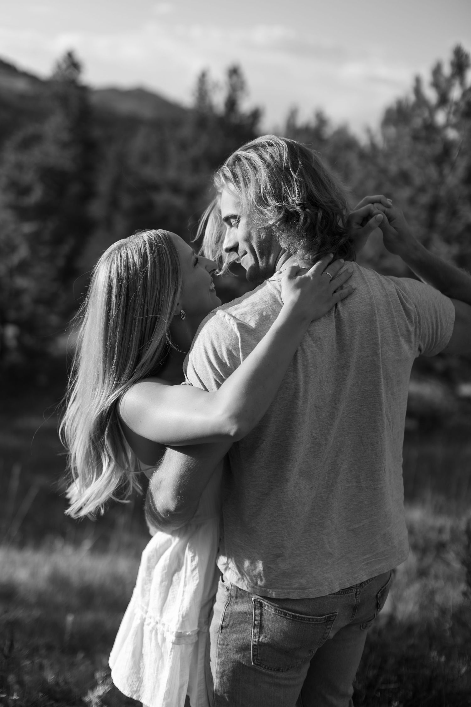 Black and white photo of a loving couple embracing closely in a natural outdoor setting with trees.