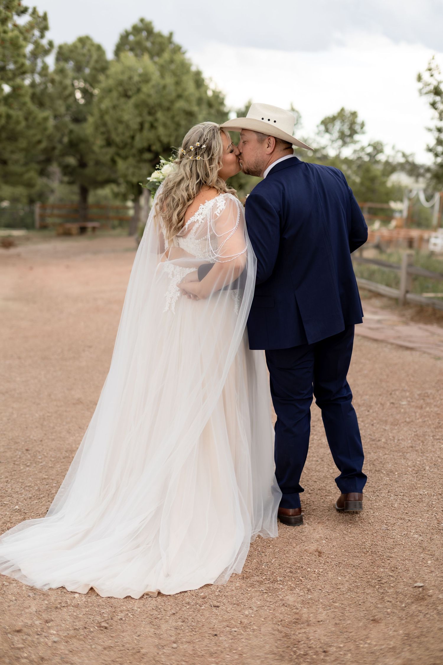 Bride and groom share a romantic kiss while walking at their rustic outdoor wedding venue.