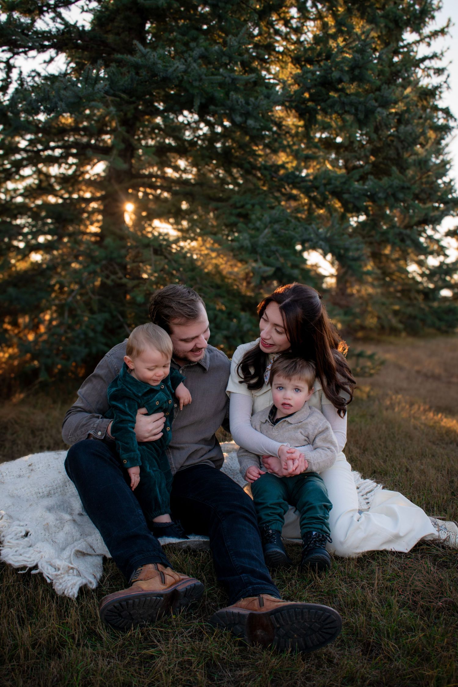 A family sits together on a grassy hillside during golden hour, sharing intimate moments and laughter.