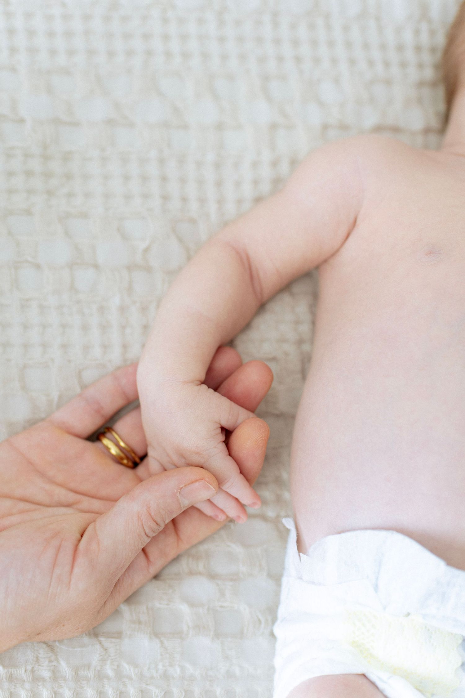 A close-up series of hands gently holding a baby's tiny hand against a soft white textured background.