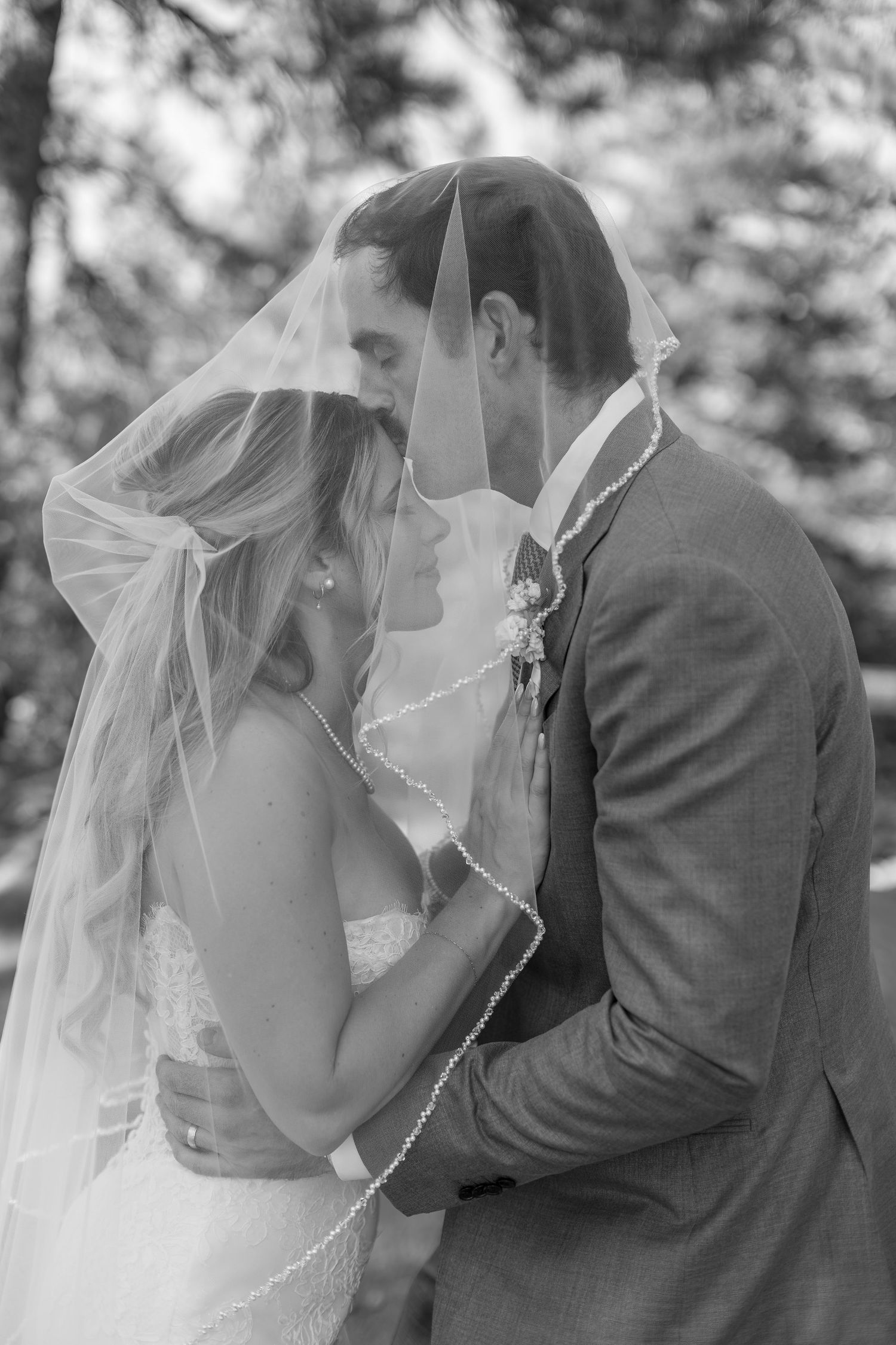 Black and white wedding photo of bride and groom sharing an intimate moment under a veil outdoors.