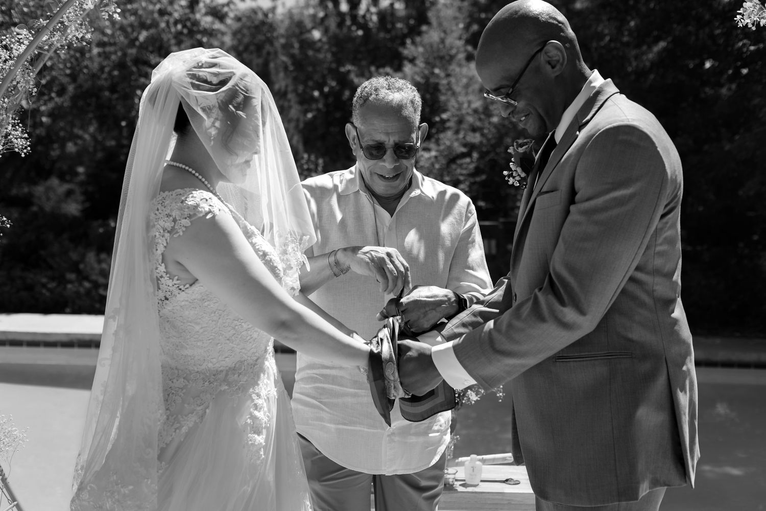 Bride and groom exchange vows with officiant in black and white outdoor wedding ceremony photo.