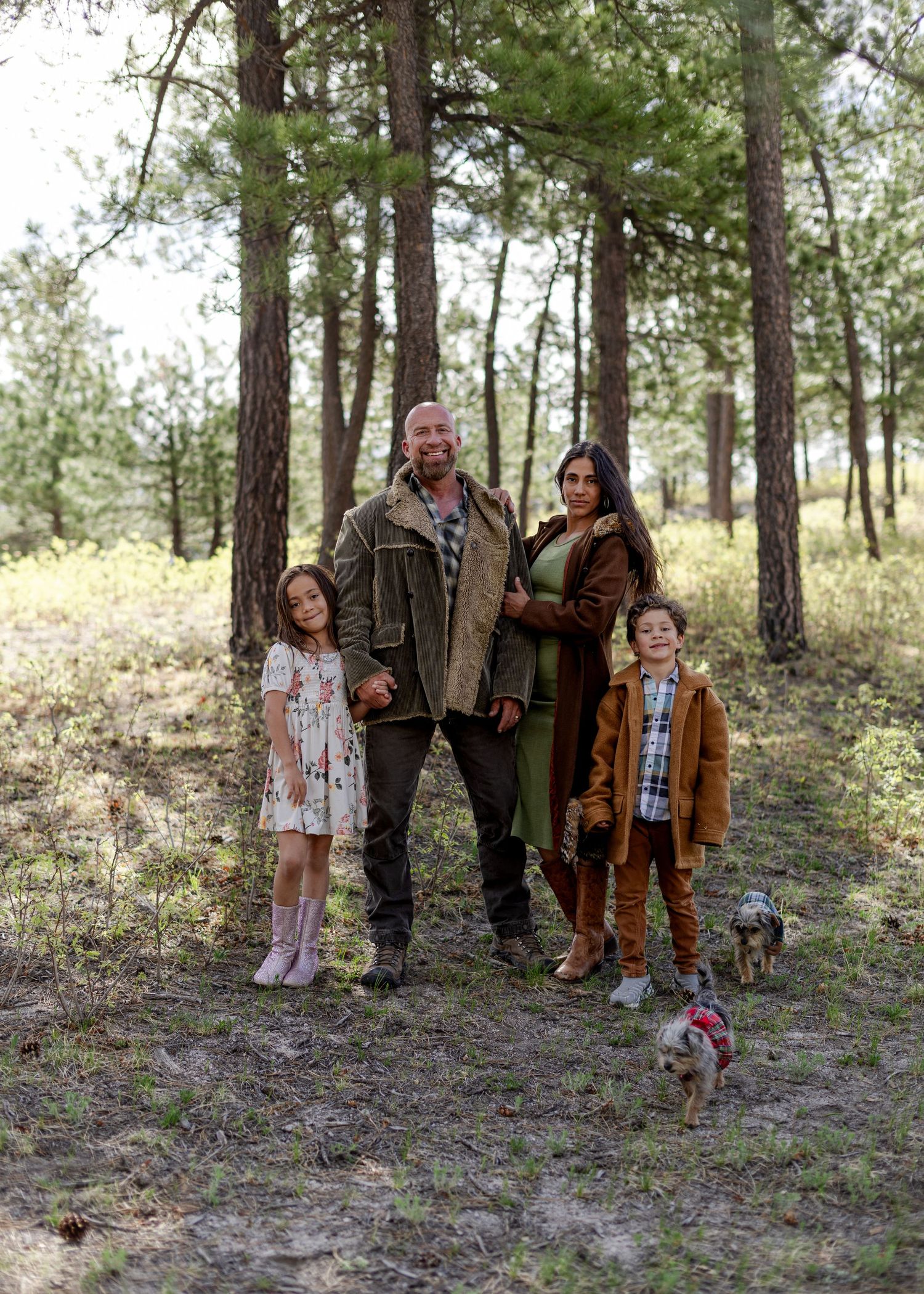 Family of four with a dog posing in a pine forest, wearing earth tones and casual outdoor attire.