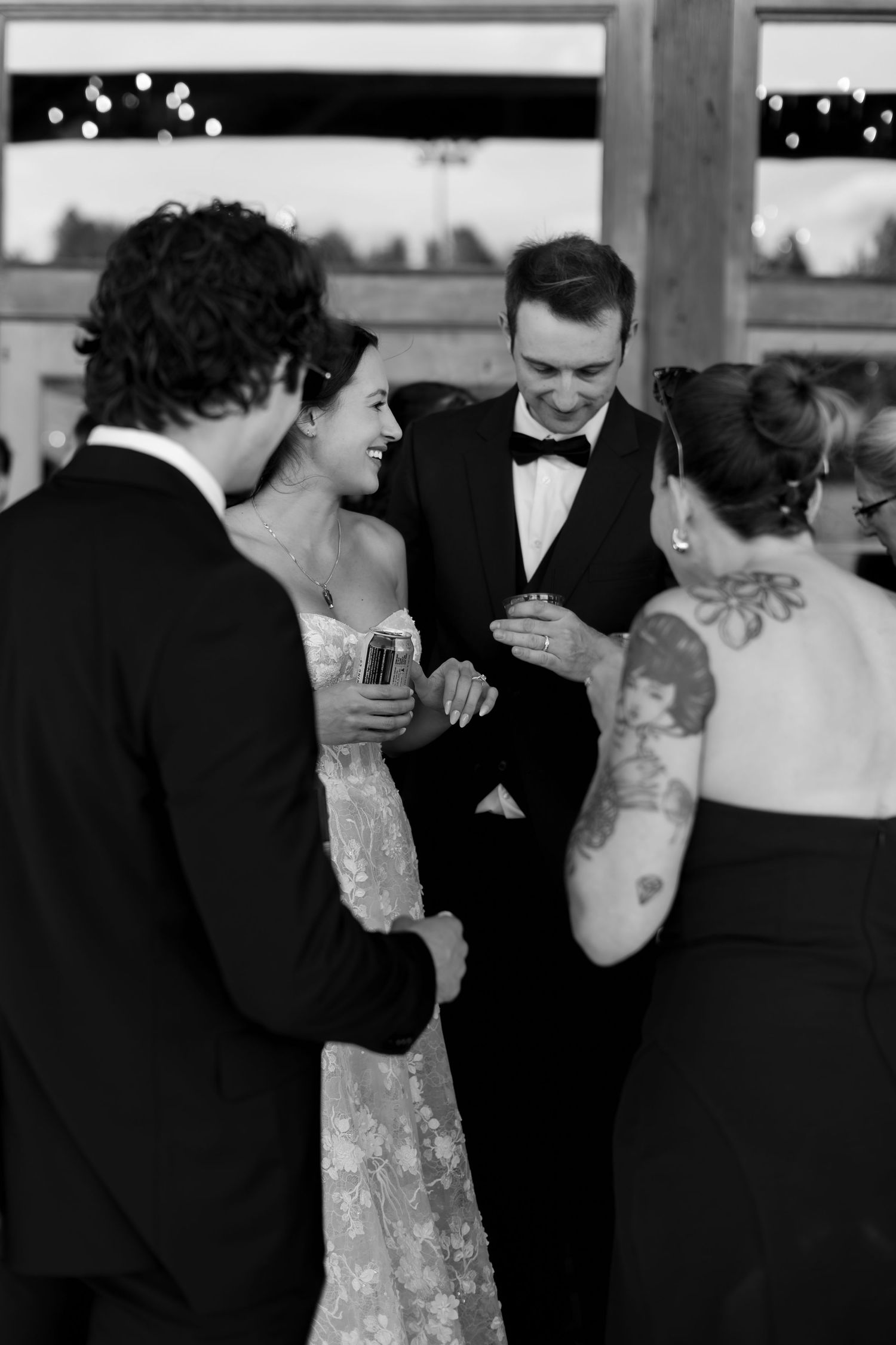 Black and white photo of a bride and groom laughing with guests at a wedding reception.