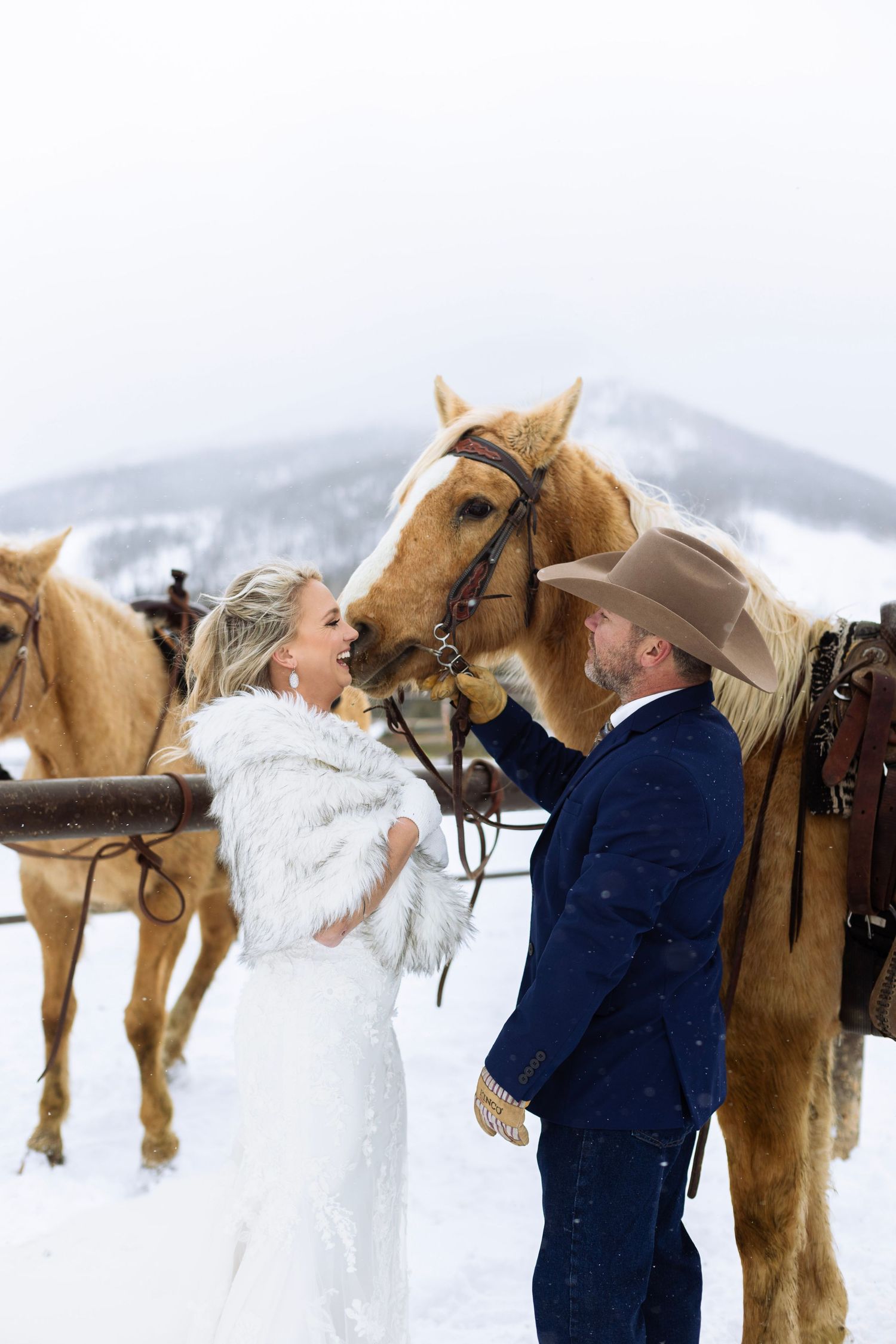 A couple shares an intimate moment with their horses during their snowy winter wedding photoshoot.