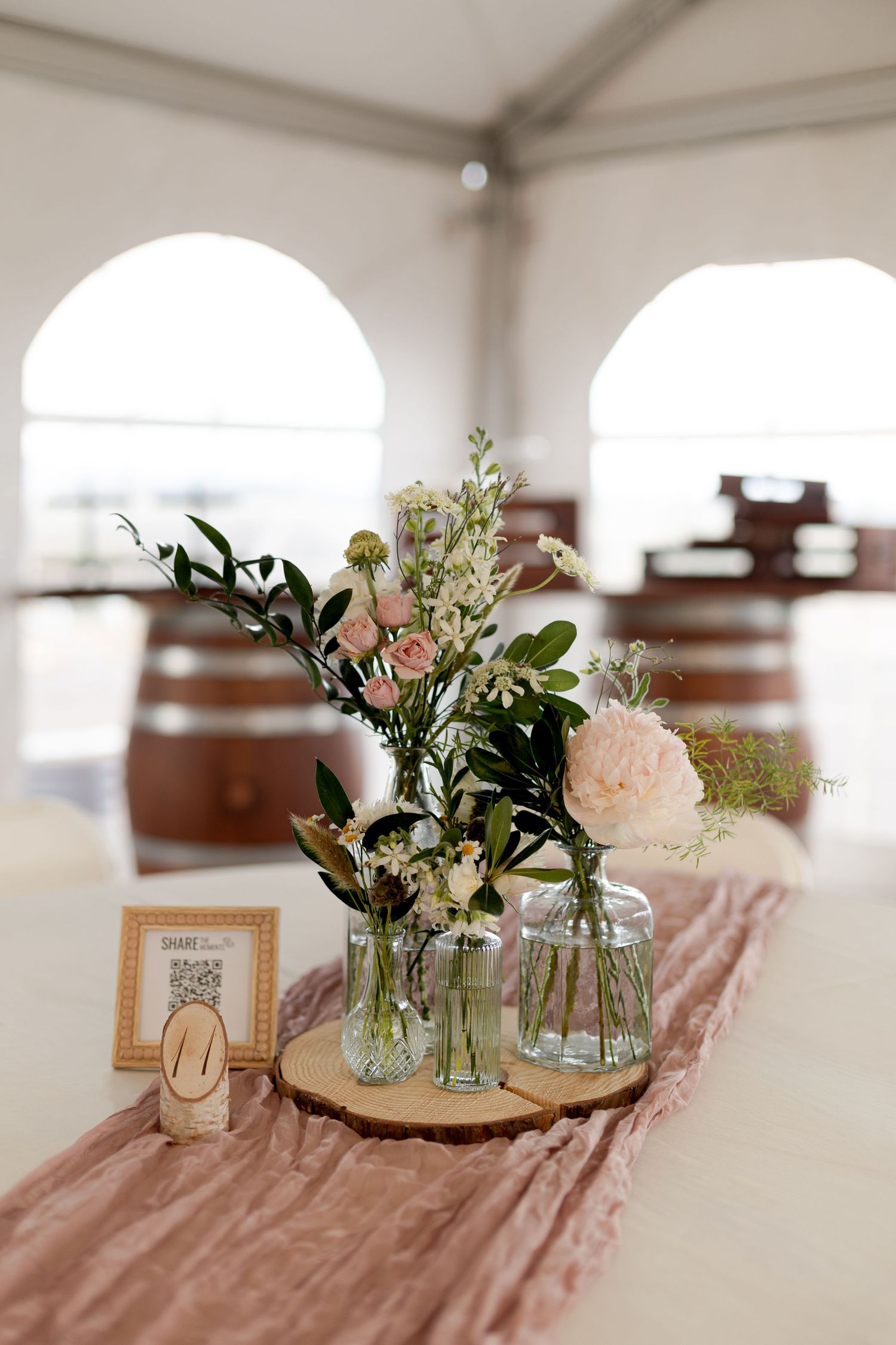 Elegant wedding reception table with blush runner, floral arrangements in glass vases on wood slice.