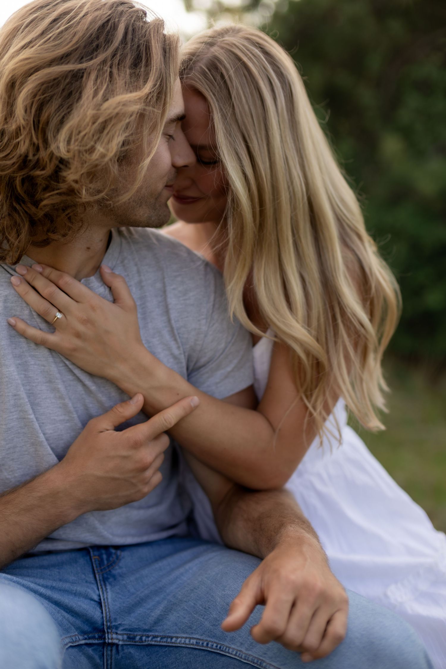 An intimate close-up of a couple nearly kissing outdoors, surrounded by lush greenery.