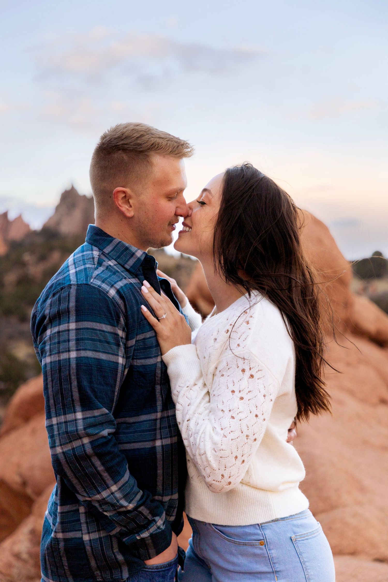 Couple sharing a romantic kiss at Garden of the Gods, Colorado, with red rock formations at sunset.