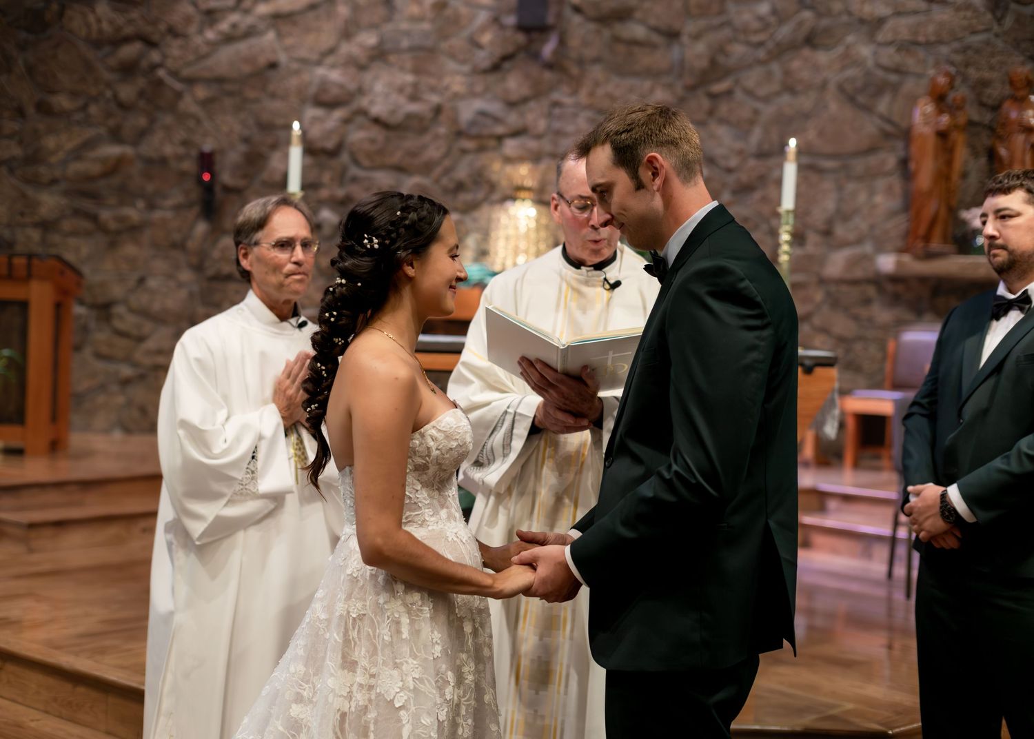Bride and groom exchange vows at stone church altar with officiant during elegant wedding ceremony.