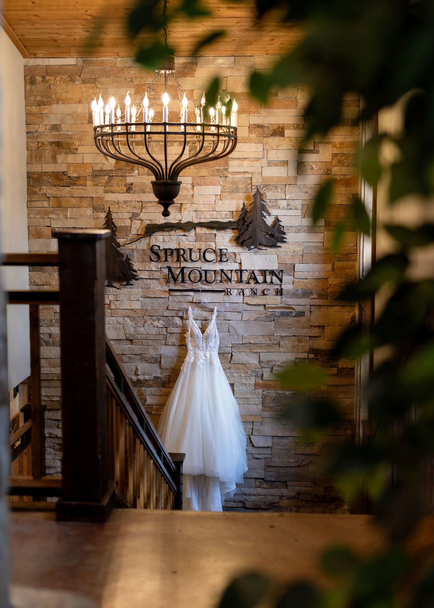 Wedding dress hanging at Spruce Mountain Ranch venue entrance with rustic stone wall and elegant chandelier.