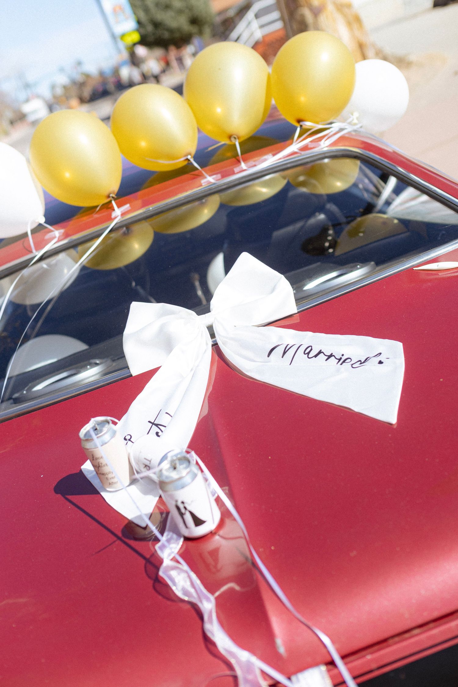 A decorated red wedding car with gold and white balloons and a white bow reading Married.