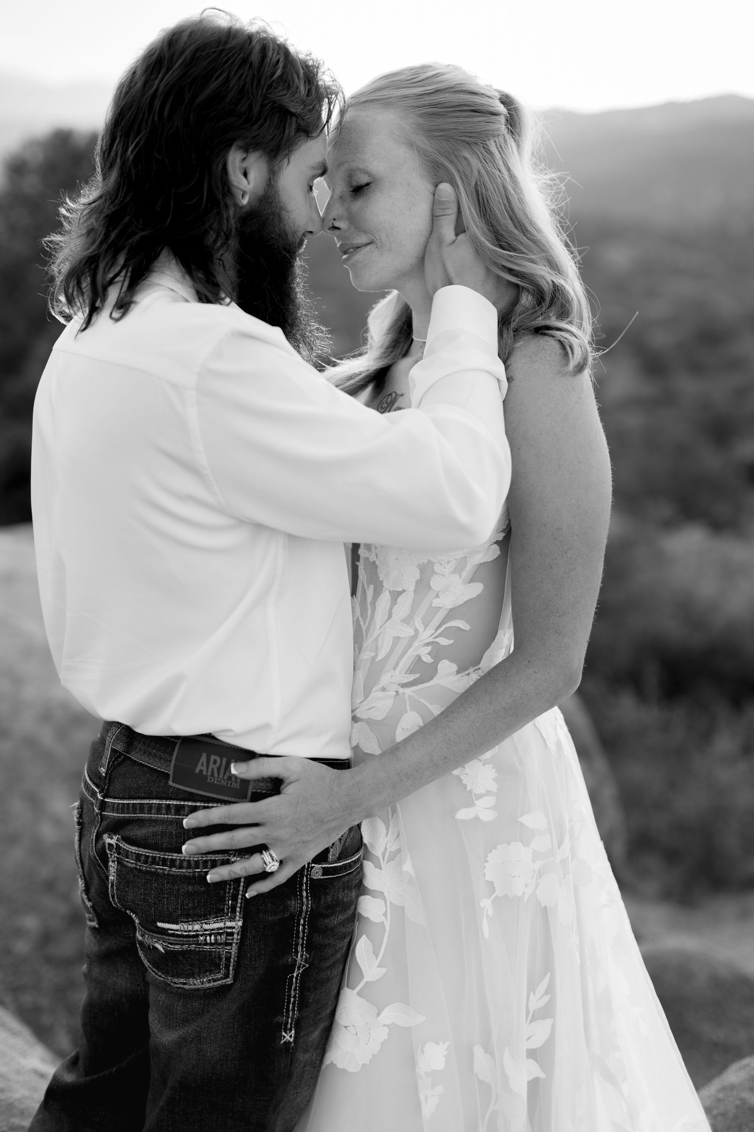 Black and white photo of bride and groom sharing intimate moment, groom tenderly holding brides face outdoors.