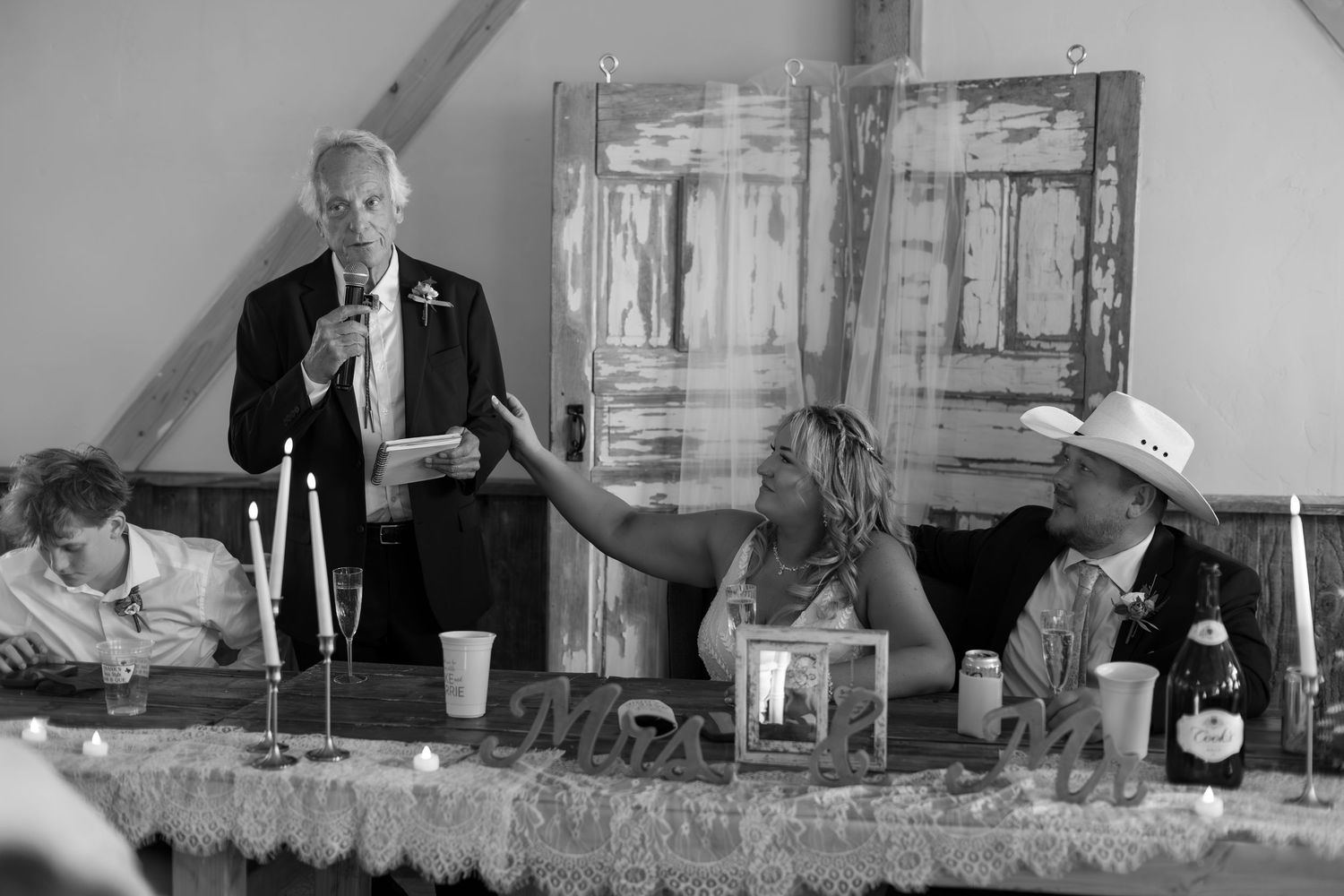 Black and white wedding reception photo showing guests at head table during a heartfelt toast speech.