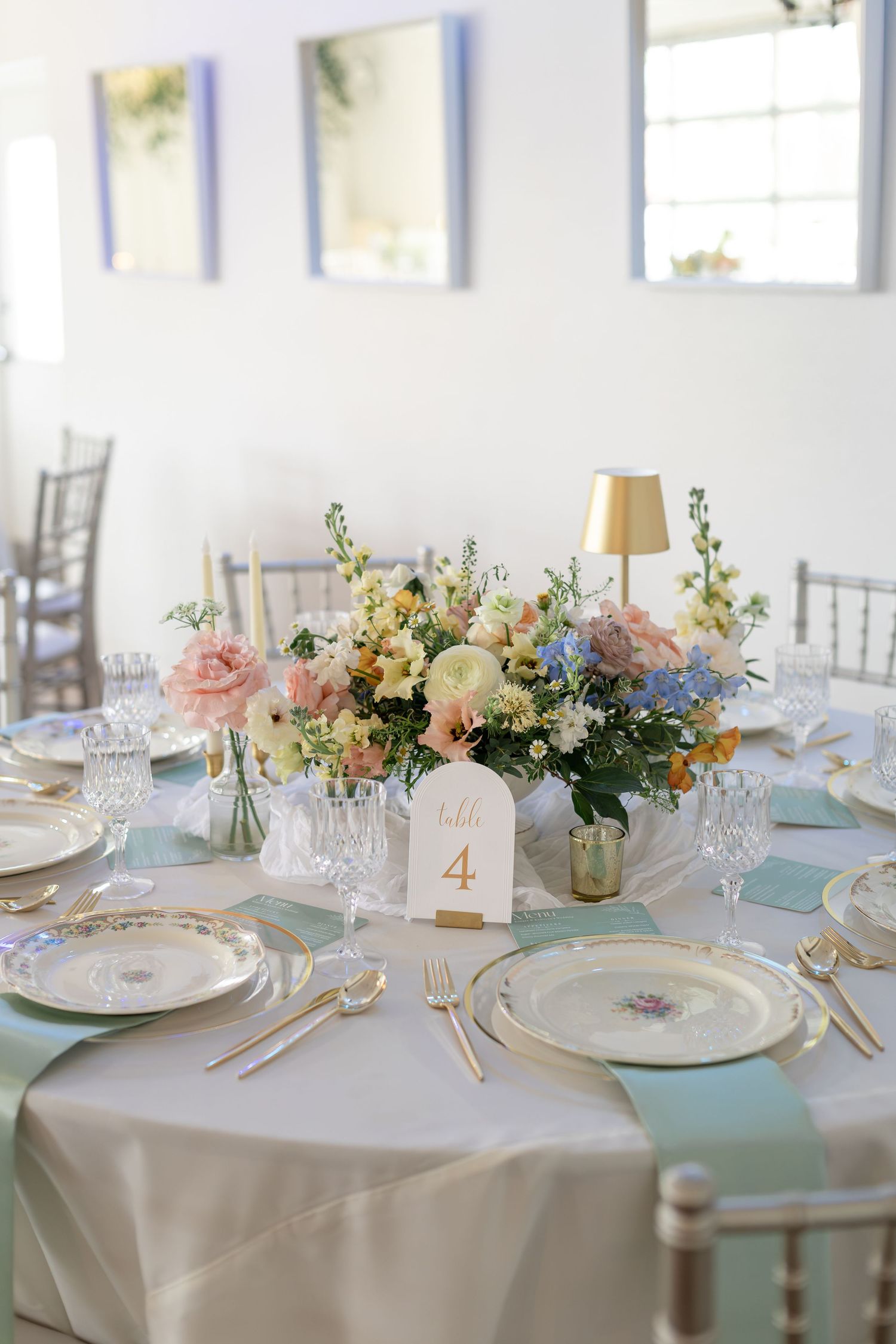 Wedding reception table 4 featuring pastel floral centerpiece, mint napkins, gold cutlery, and crystal glassware.