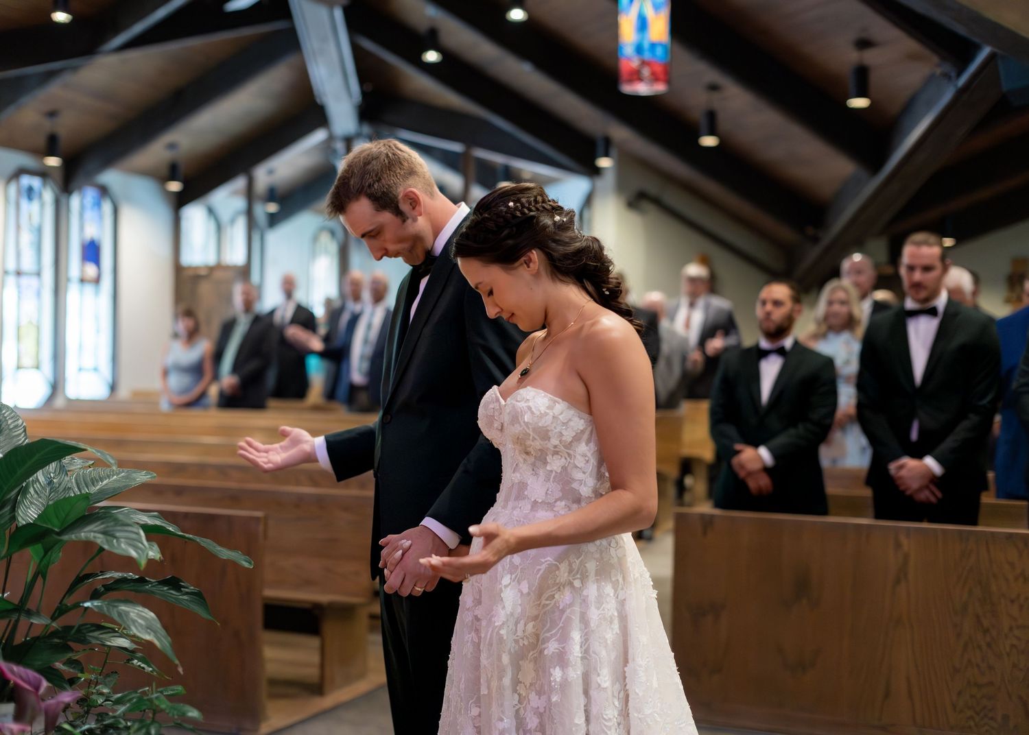 Bride and groom holding hands at church altar during wedding ceremony, guests seated in pews behind them.