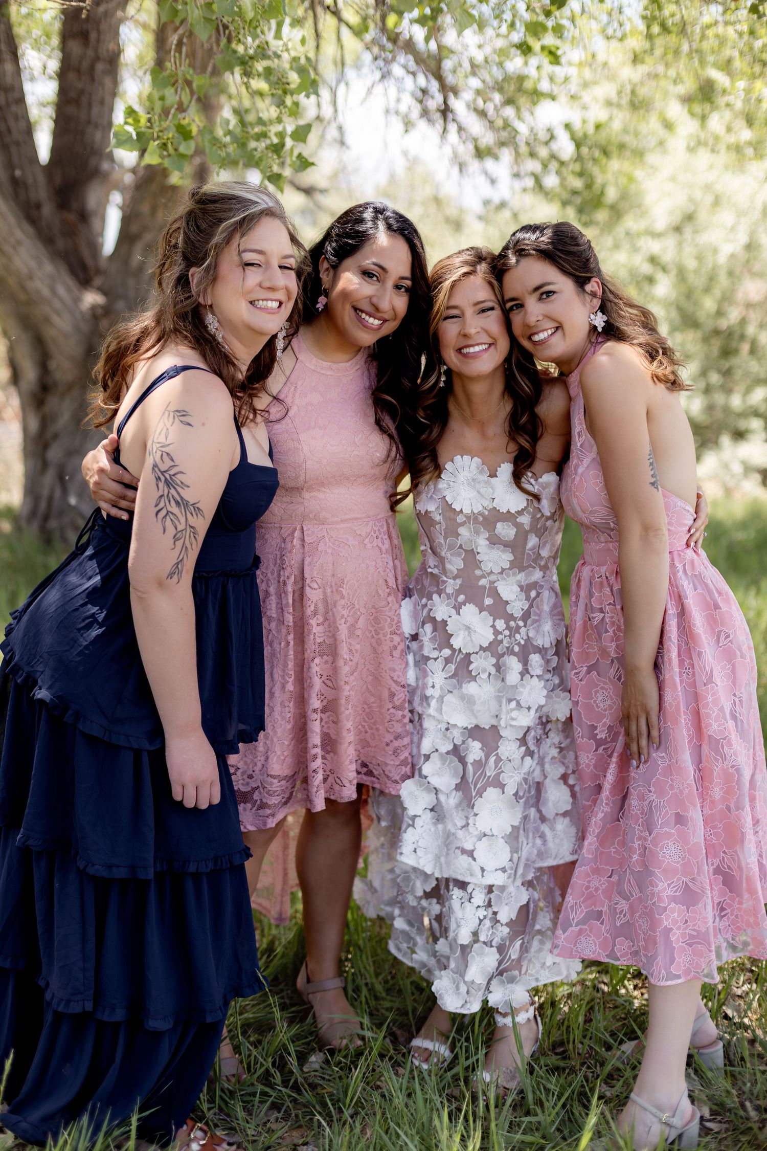Four women in pink and navy dresses smiling together at an outdoor wedding celebration.