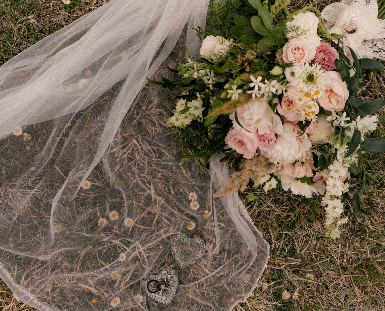 Bridal veil with floral details laid beside a romantic pink and white wedding bouquet on grass.