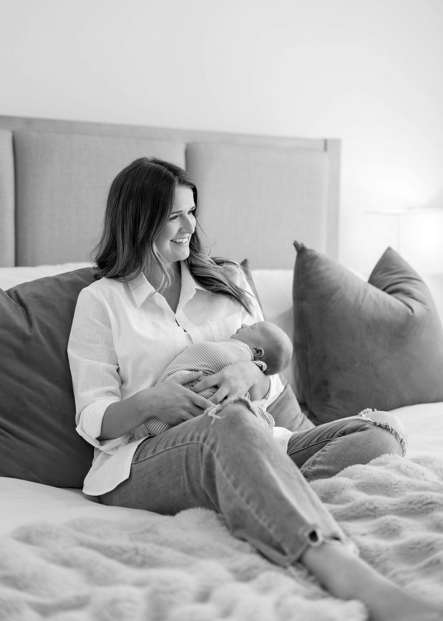 Black and white photo of a smiling mother sitting on a bed cradling her newborn baby.