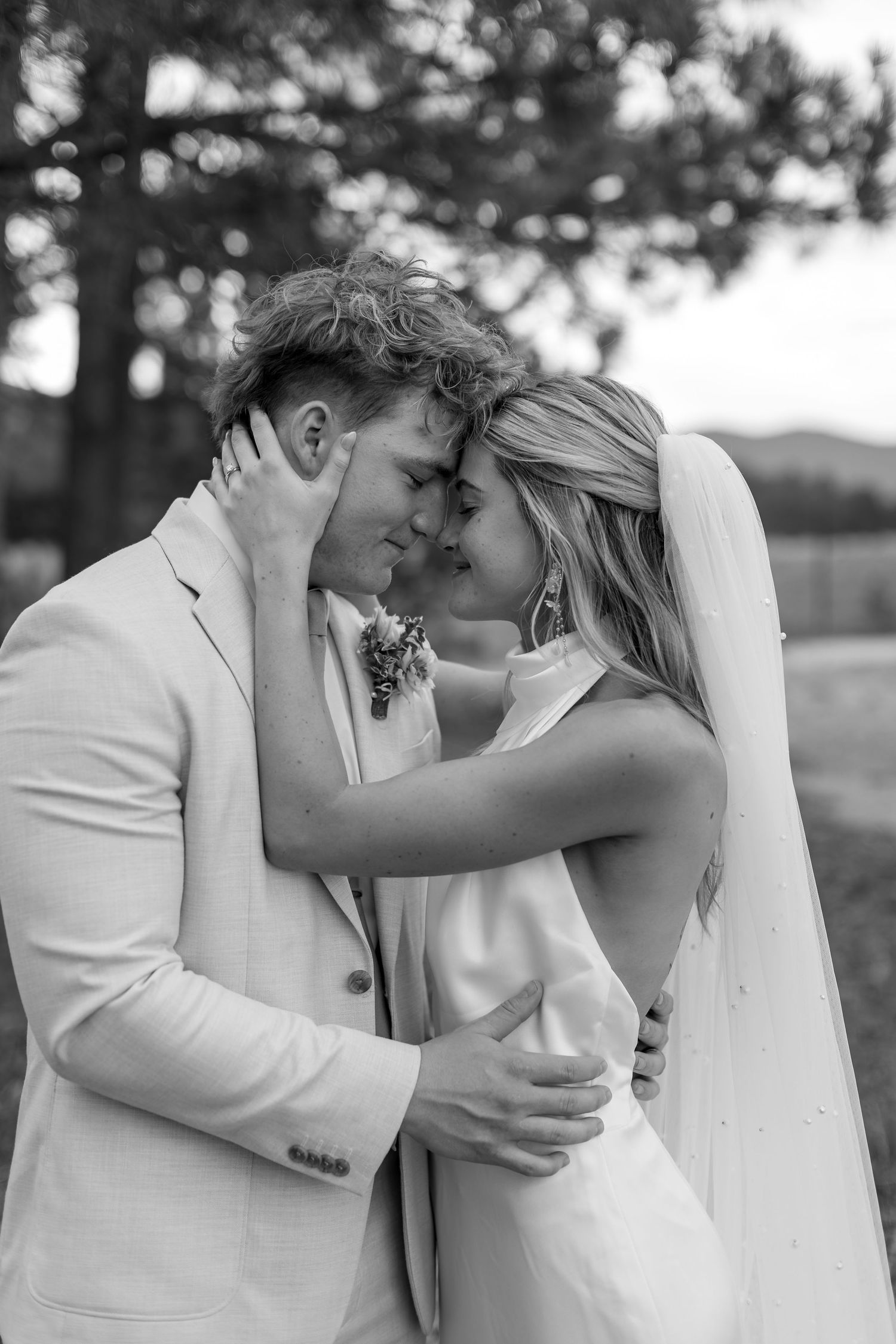 Black and white photo of bride and groom sharing tender forehead touch in outdoor forest setting.