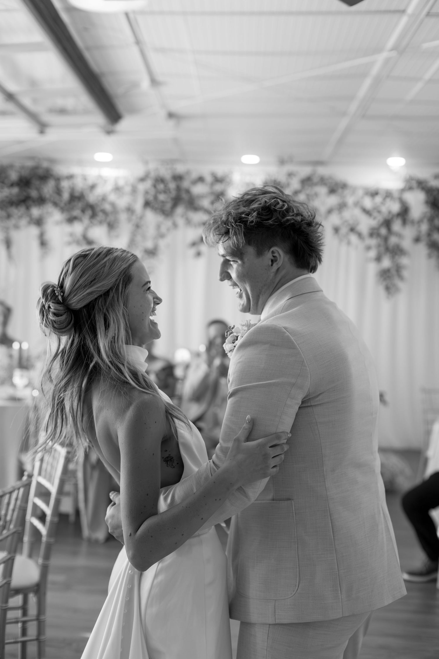 Black and white photo of a bride and groom sharing their first dance at a wedding reception.